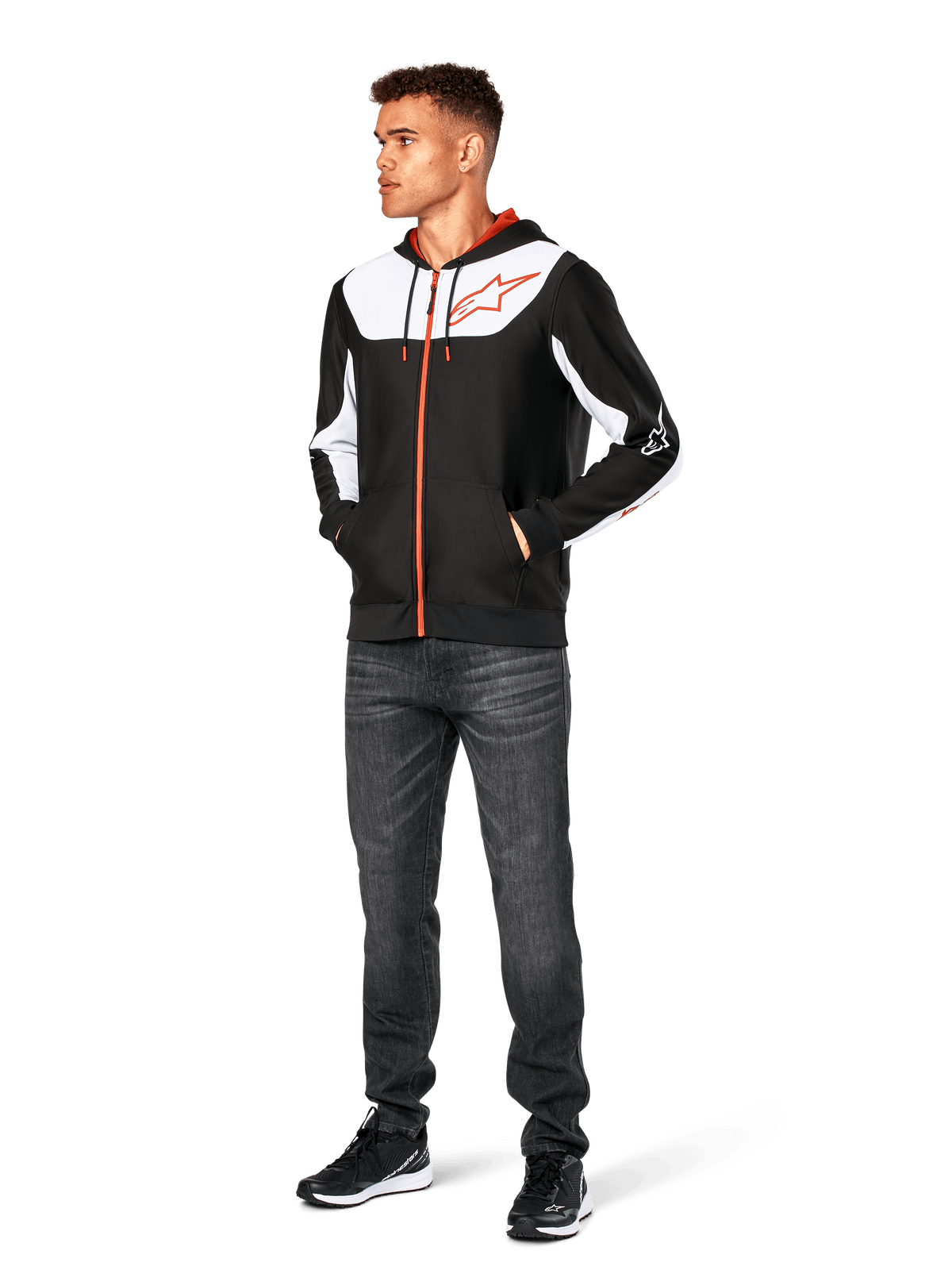 Alpinestars Sessions V3 Hoodie, lässige Kapuzenjacke mit Reißverschluss, Schwarz, Weiß und Rot, getragen von einem Model mit dunkler Jeans und schwarzen Sneakern, mit weißen Color-Block-Einsätzen an Brust und Ärmeln, rotem Reißverschluss und Kordelzug, großem Brustlogo, Poly-Fleece, vom Motorsport inspirierte Streetwear