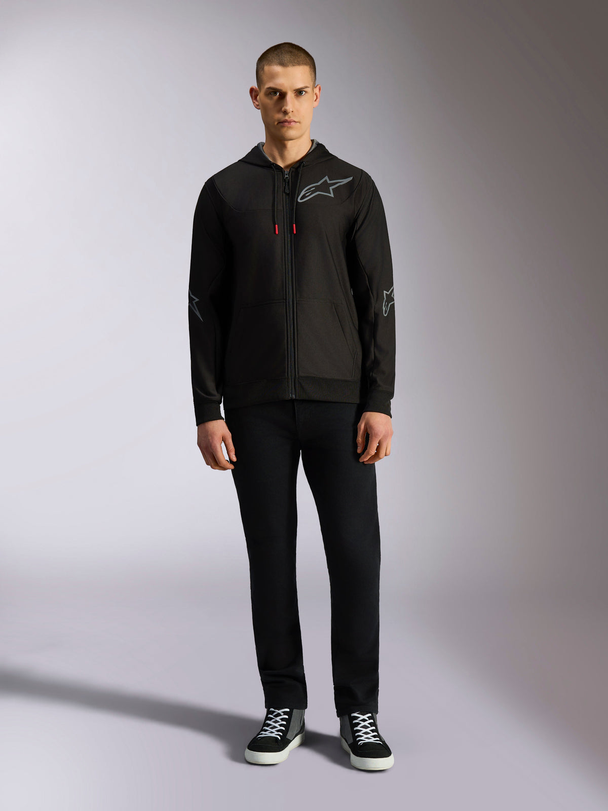 Alpinestars Sessions V3 Hoodie, Kapuzenjacke mit Reißverschluss aus Fleece, Schwarz mit grauem Astars-Logo auf der Brust und den Ärmeln, Kordelzüge mit roten Enden, lässige, vom Motorsport inspirierte Streetwear.
