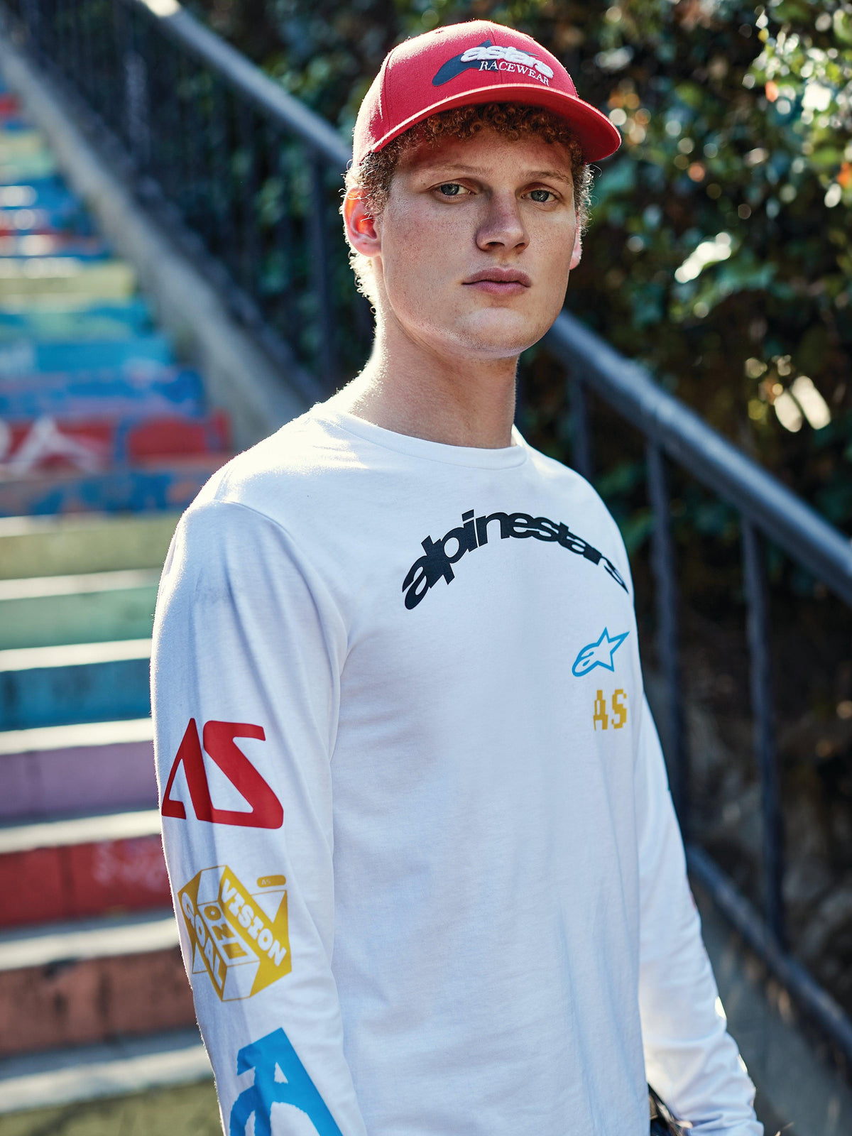 Alpinestars Profile Hat, Red, worn by a young man, structured crown with curved bill and embroidered logo, paired with a white graphic long-sleeve T-shirt, casual motorsport streetwear