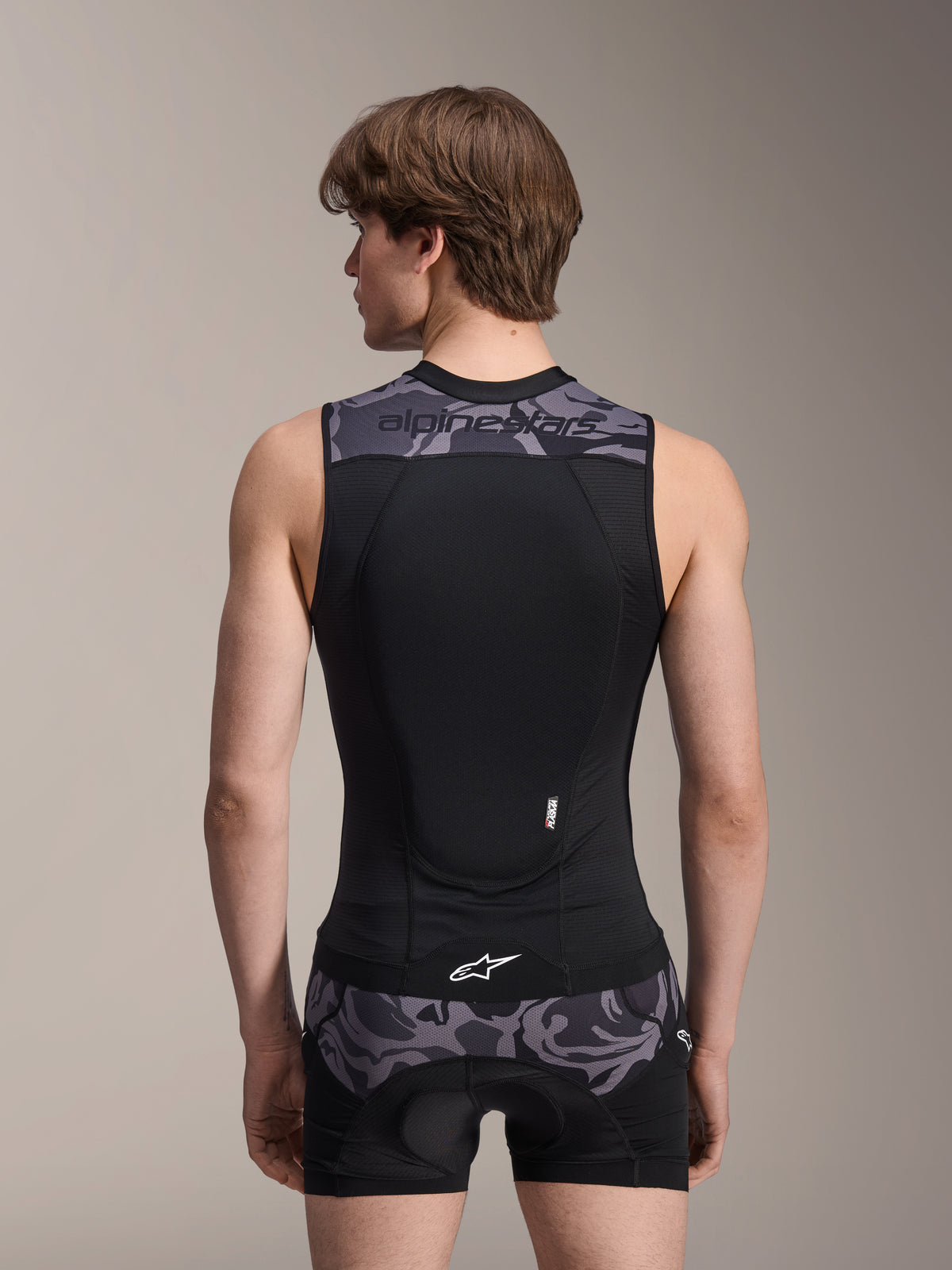 Alpinestars A-Motion Plasma Schutzweste, Black Camo, Rückansicht an einem männlichen Model, mit atmungsaktiver Mesh-Konstruktion und integriertem Nucleon Plasma Rückenprotektor, graue Camouflage-Akzente an den Schultern und der Taille sowie Alpinestars-Branding.