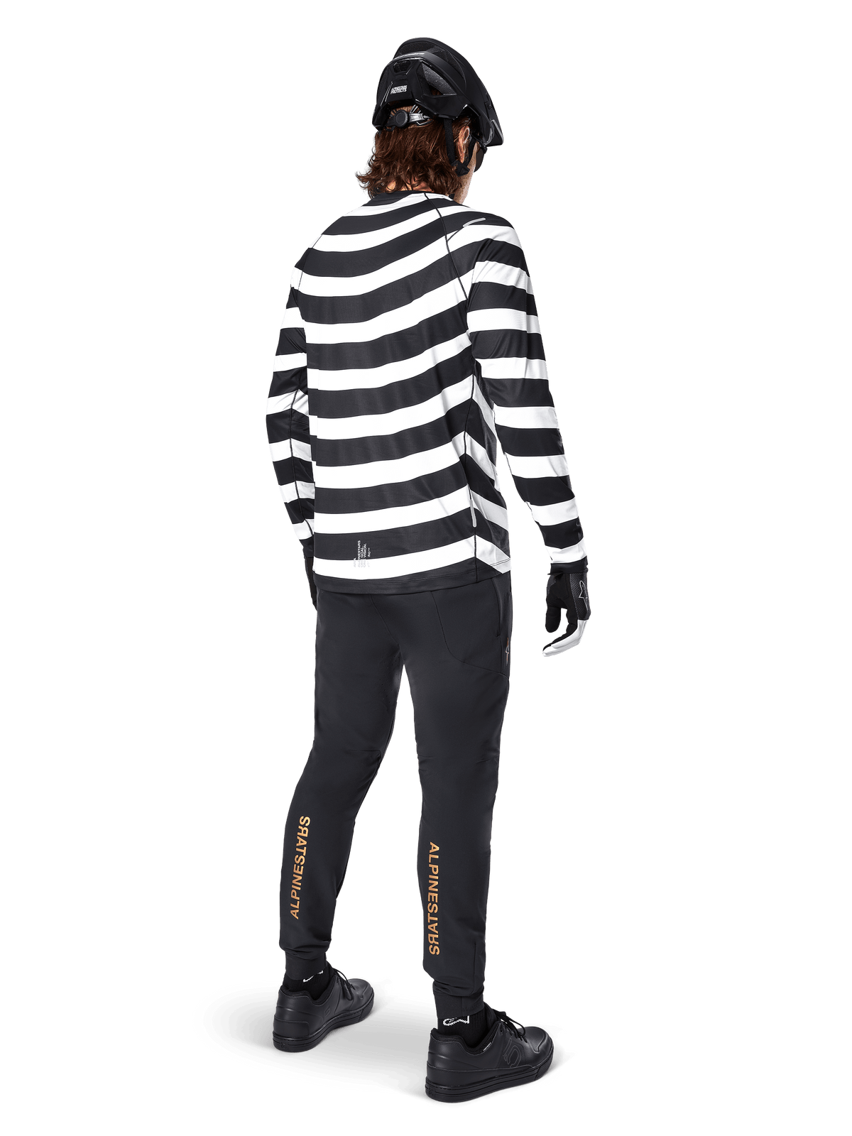Alpinestars A-Aria Elite Pants, Black MTB Pants, featuring gold vertical logo on the calves, worn by a rider with a black and white striped long-sleeve jersey, black helmet, and black shoes, rear view showing performance fit and trail-ready design