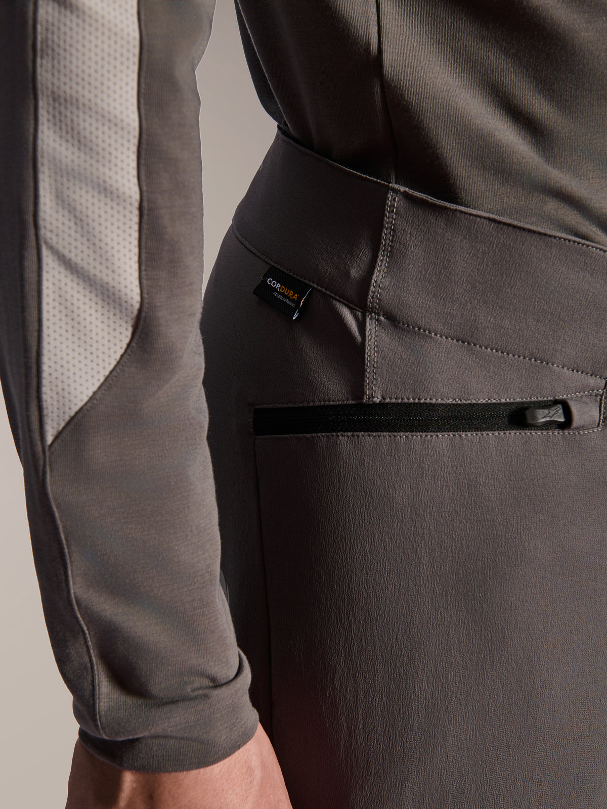 Alpinestars A-Dura Elite Pants, dunkelgraue Mountainbike-Hose, Detailansicht der seitlichen Reißverschlusstasche und des Cordura-Stoffetiketts, strapazierfähiges 4-Wege-Stretch-Textil für Offroad-Performance