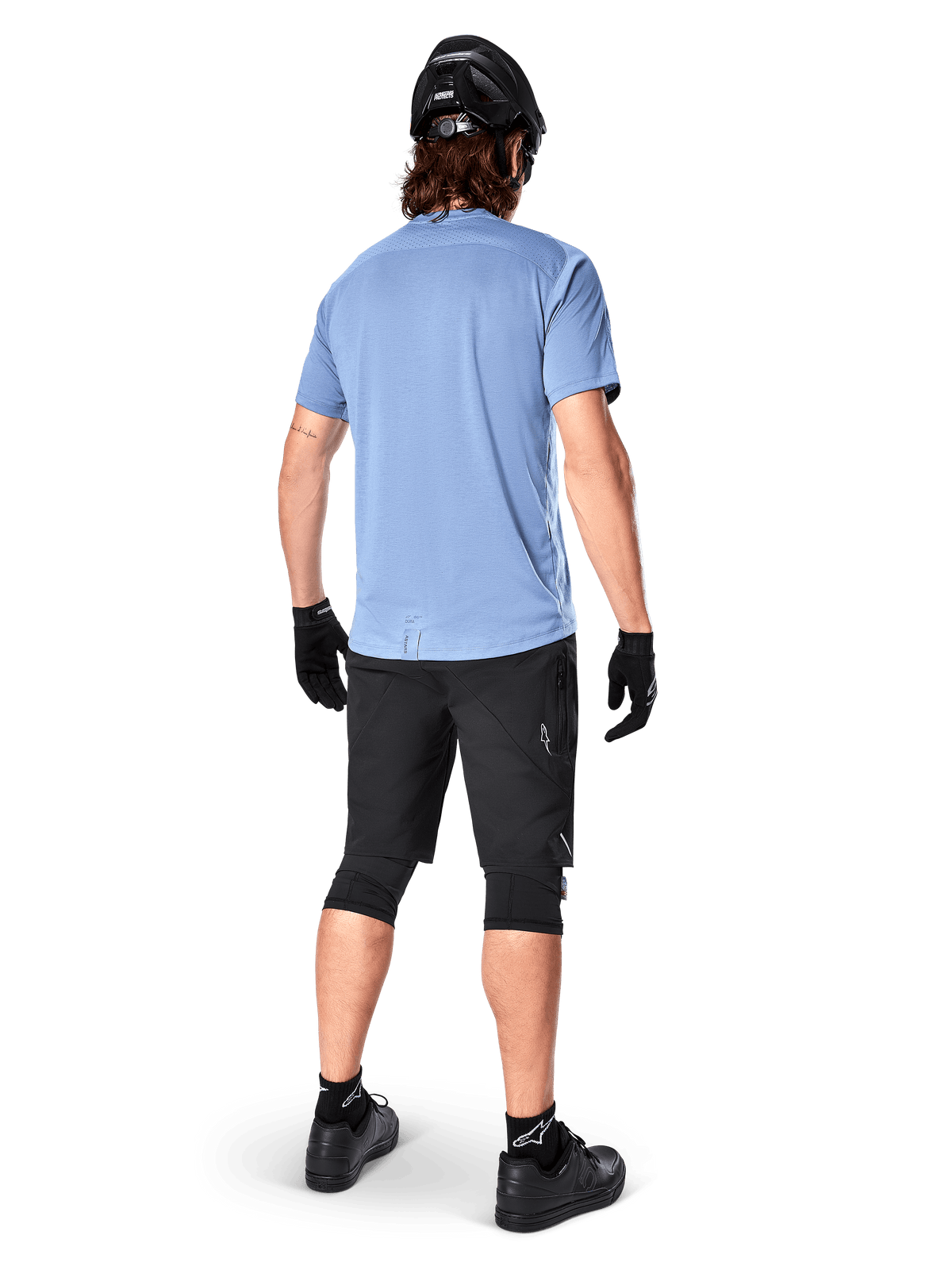 Alpinestars A-Dura Elite Shorts, Mountainbike-Shorts, Schwarz, Rückansicht am Model, getragen mit hellblauem Kurzarmshirt und schwarzer Schutzausrüstung, technisches Design mit Reißverschlusstaschen und reflektierenden Details für den Offroad-Radsport