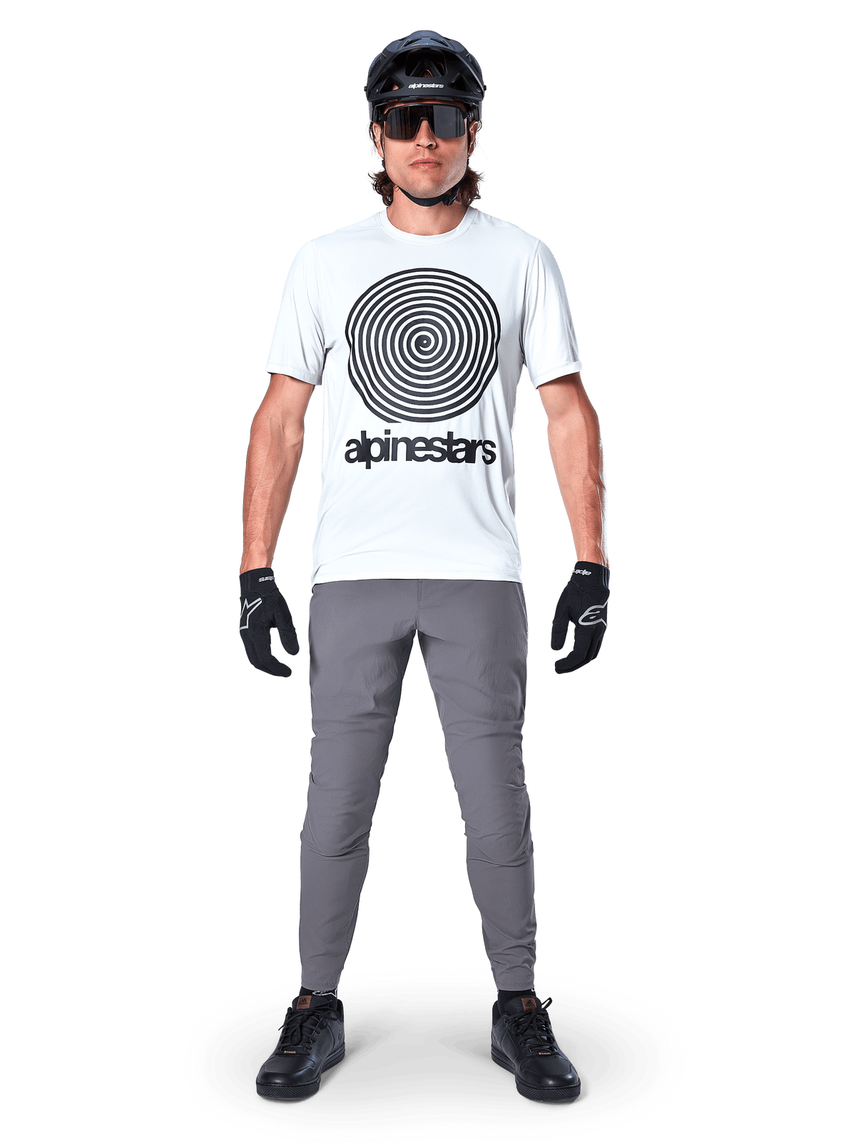 Alpinestars A-Dura Hose, MTB-Hose, Dunkelgrau, getragen mit einem weißen Grafik-T-Shirt, schwarzem Helm und Handschuhen, strapazierfähiges 2-Wege-Stretch-Design und reguläre Passform für Mountainbiking