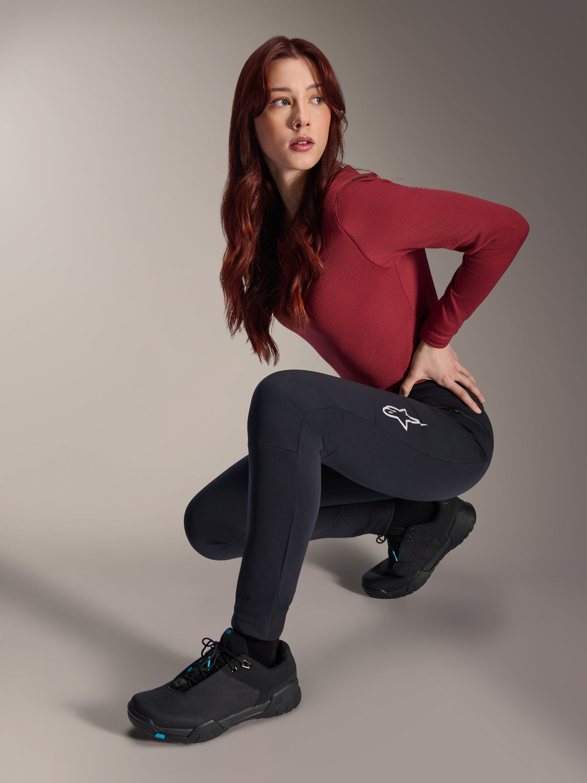 Alpinestars Stella A-Dura Thermohose, MTB-Hose für Damen, Schwarz, getragen von einem Modell in hockender Pose mit einem weinroten Langarmshirt und schwarzen Radschuhen, mit weißem Stern-Logo auf dem Oberschenkel, strapazierfähige und warme Konstruktion für Geländefahrten bei kaltem Wetter