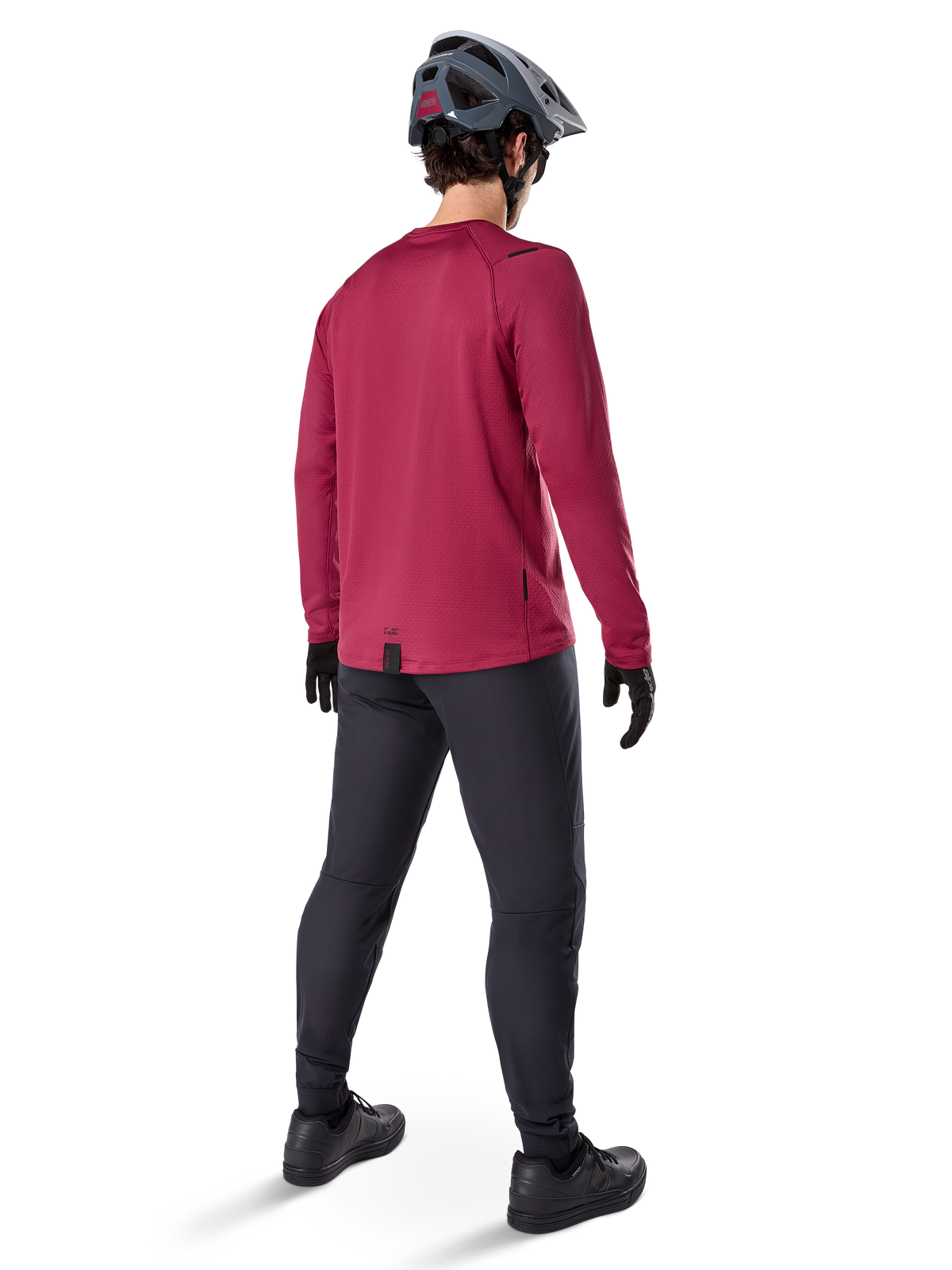 Alpinestars A-Dura Thermal Jersey, Burgundy long-sleeve cycling jersey, back view, worn with black mountain bike pants and a grey helmet, featuring an extended drop tail hem for rear coverage, mountain bike gear for cold weather