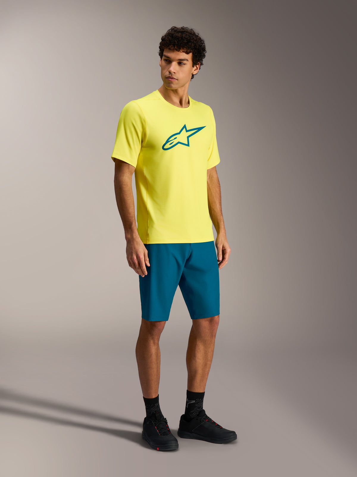Alpinestars A-Dura Ride MTB outfit featuring a yellow short-sleeve jersey and teal blue-green shorts on a male model.