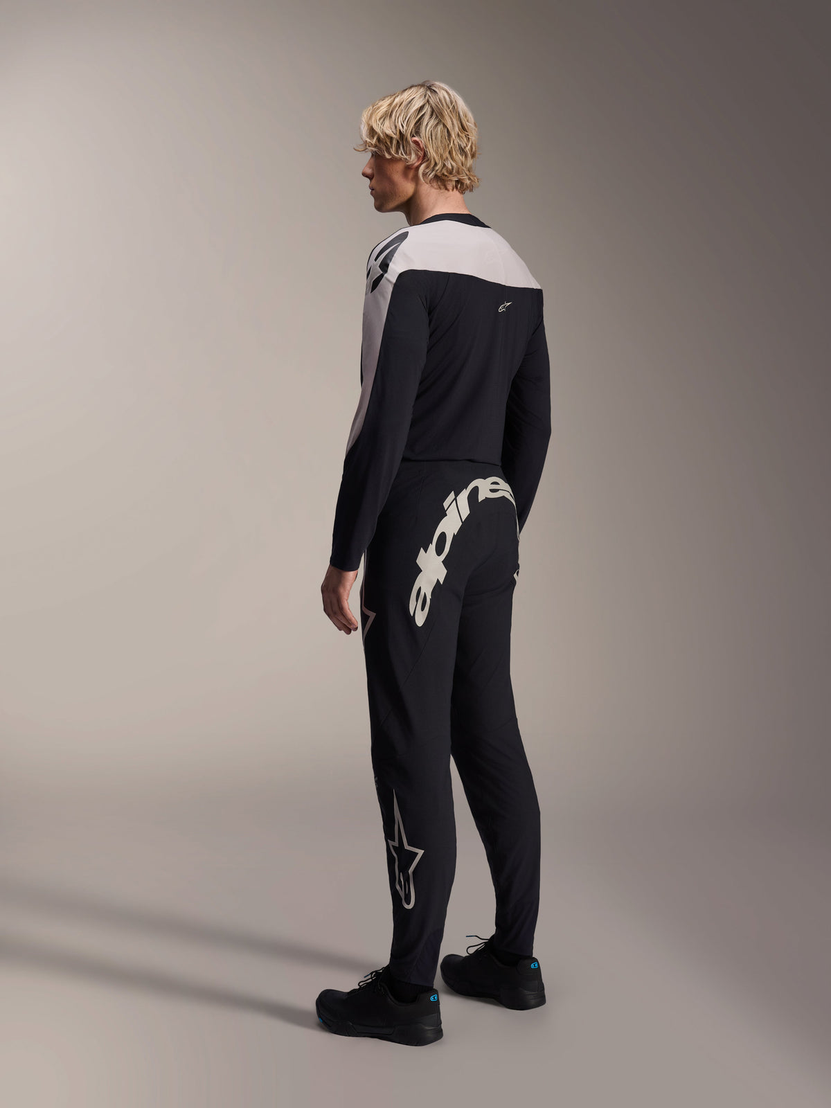 Alpinestars A-Supra Melt Hose, MTB-Hose, Schwarz, mit einem großen weißen Alpinestars-Schriftzug auf der Rückseite und Stern-Logo am Bein, getragen von einem Modell mit einem passenden langärmeligen Trikot und schwarzen Schuhen, Rückansicht