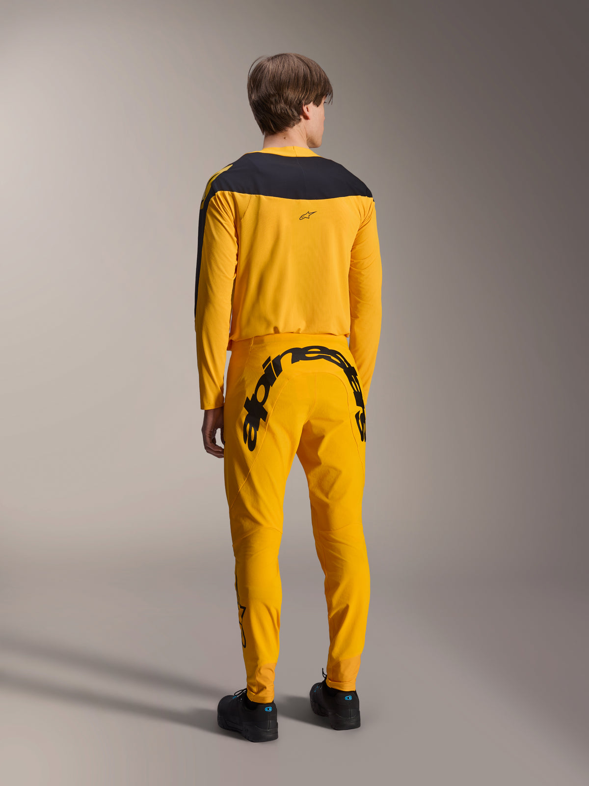 Alpinestars Limited Edition A-Supra Melt Gold Ausrüstungsset, MTB-Trikot und Hose, Dunkelgelb und Schwarz, Rückansicht mit großem Alpinestars-Schriftzug auf dem Gesäß und schwarzer Rückenpasse am Trikot, Performance-Mountainbike-Bekleidung