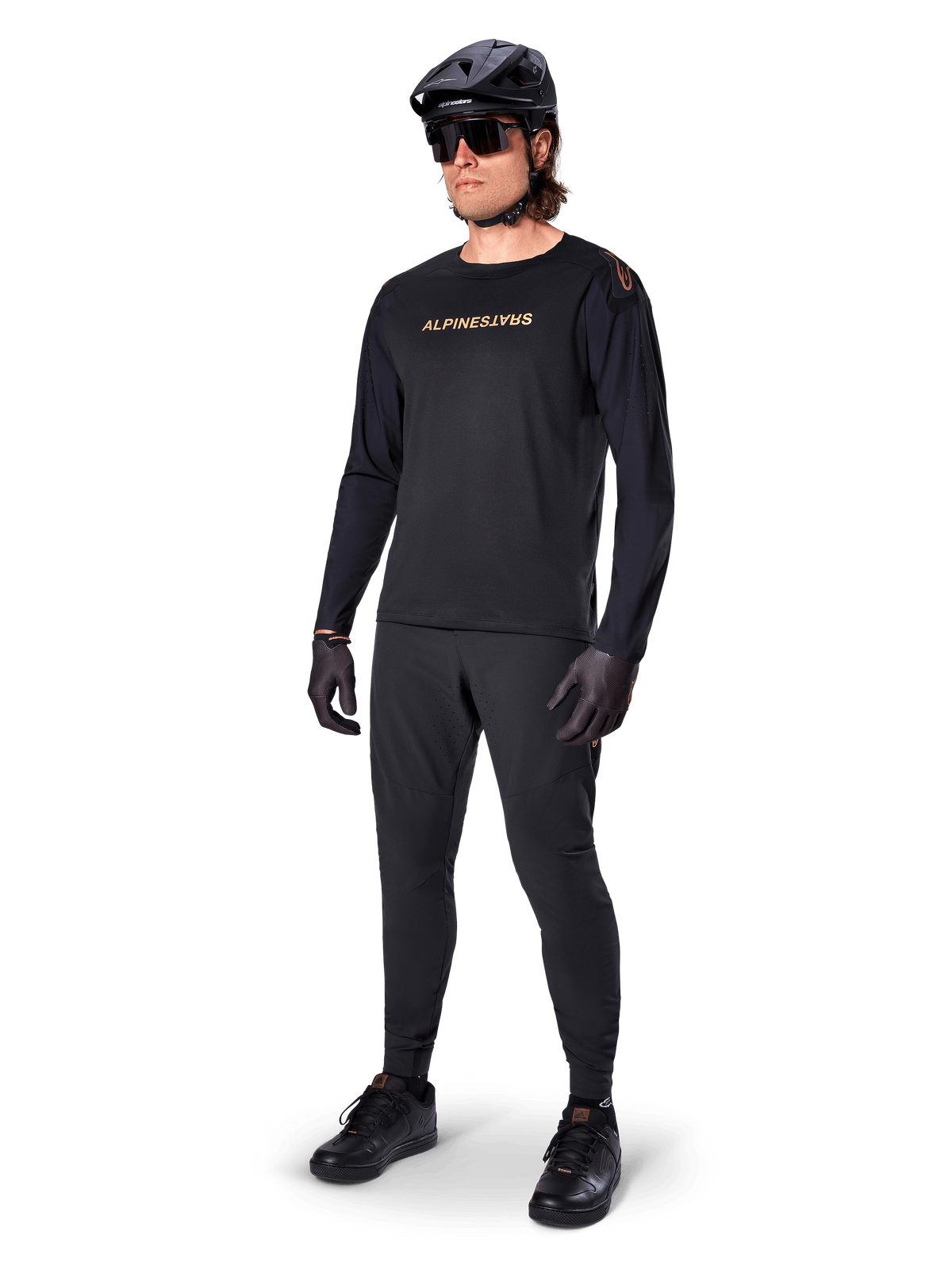 Alpinestars A-Aria Polartec Switch Langarmtrikot, Schwarz, bronzefarbenes Branding auf der Brust, getragen von einem Mountainbiker mit schwarzem Helm und Sonnenbrille, Performance-Radsportbekleidung für Trail-Fahrten