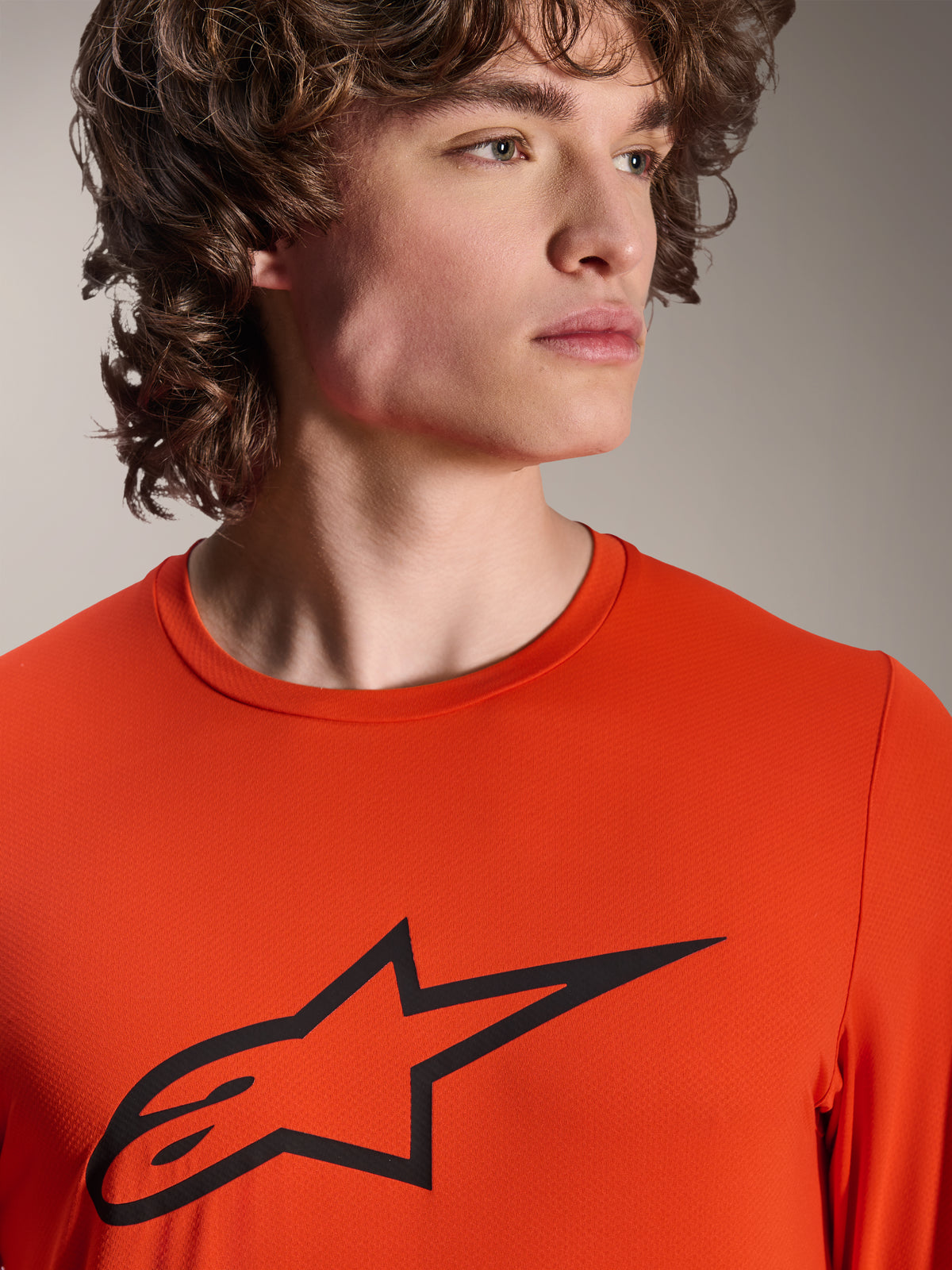 Alpinestars A-Dura Insert Astar Trikot, Langarm-MTB-Trikot, Spicy Orange, mit schwarzem Alpinestars Astar-Logo auf der Brust, Nahaufnahme an einem männlichen Model