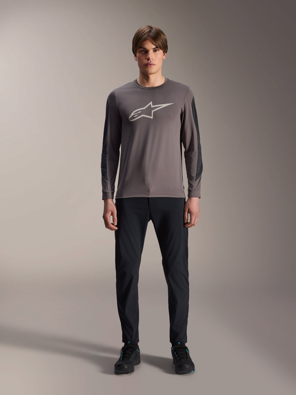 Alpinestars A-Dura Insert Astar Jersey, Langarm-MTB-Jersey, Dunkelgrau, mit auffälligem hellgrauen Astar-Logo auf der Brust und dunkleren texturierten Ärmeleinsätzen, getragen von einem Model mit schwarzer Hose und Schuhen, Performance-Ausrüstung für das Mountainbiken