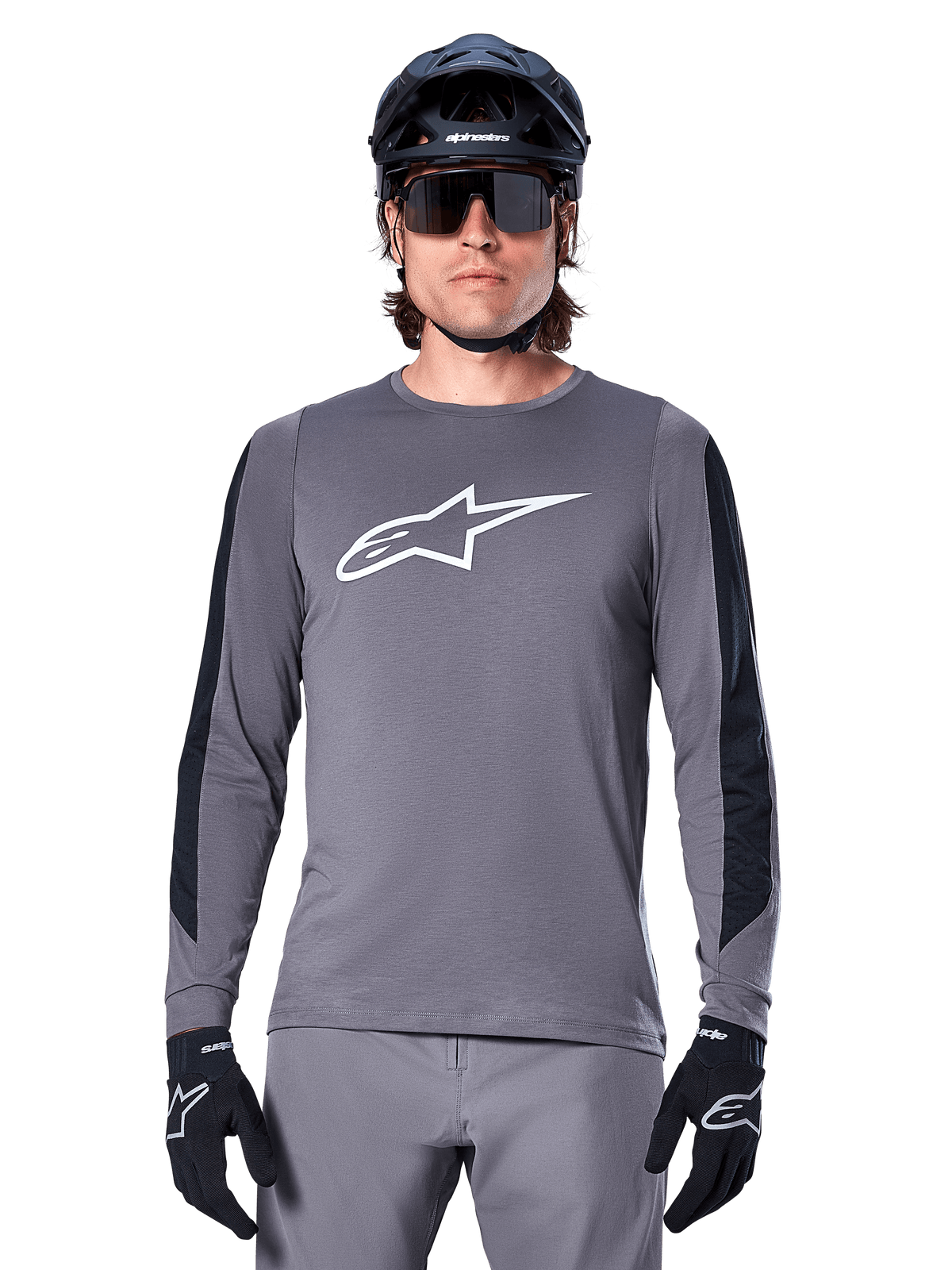 Alpinestars A-Dura Dri Astar Langarmtrikot, Dunkelgrau, mit großem weißen Astar-Logo auf der Brust und schwarzen Mesh-Einsätzen an den Armen, getragen von einem Fahrer mit schwarzem Mountainbike-Helm und Performance-Sonnenbrille, MTB-Radsportbekleidung