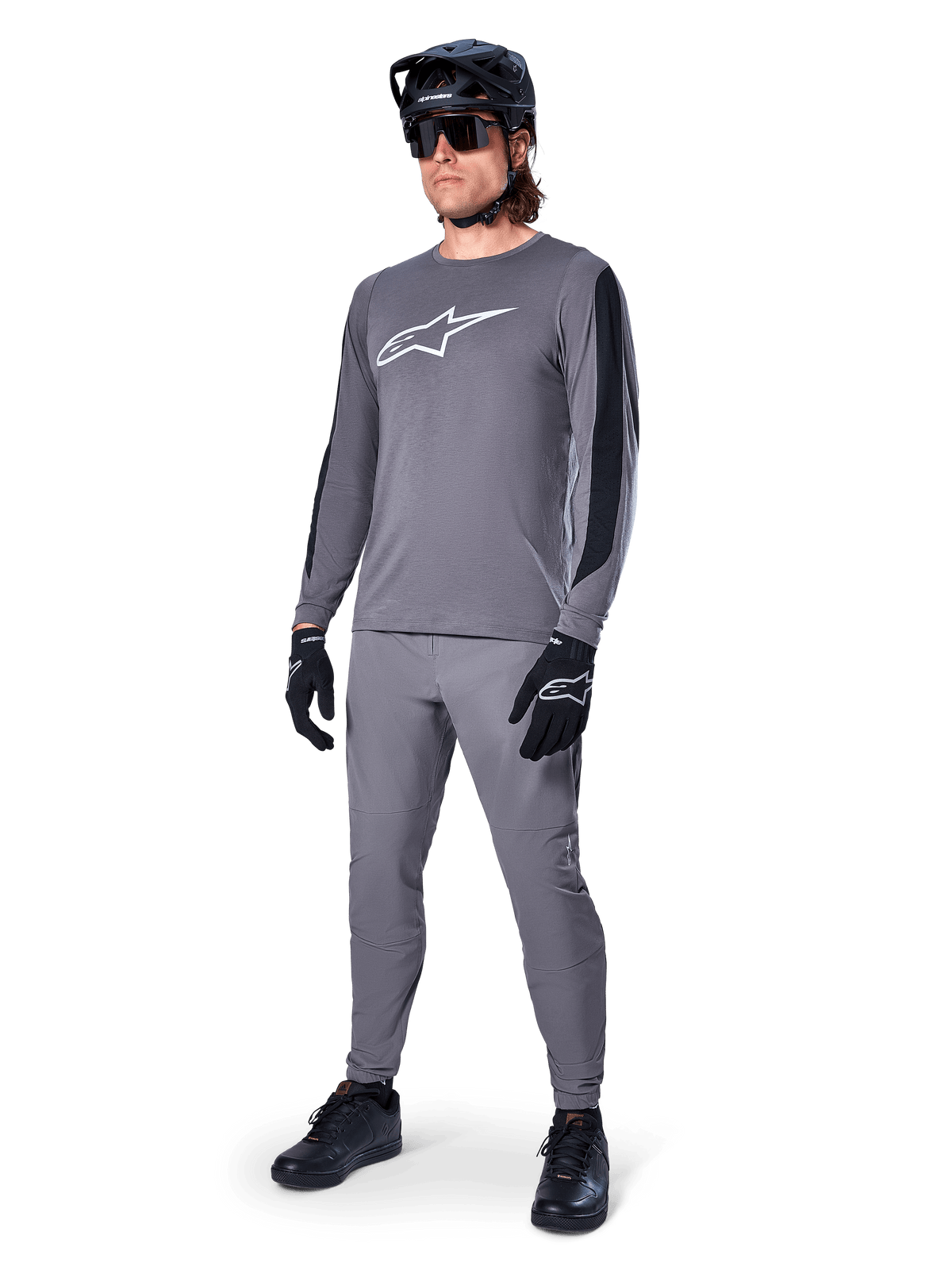 Alpinestars A-Dura Dri Astar Langarm-MTB-Trikot, Dunkelgrau mit weißem Brustlogo, schwarze Mesh-Einsätze an den Ärmeln, kombiniert mit passender grauer Hose, schwarzem Helm und Handschuhen, Performance-Mountainbike-Bekleidung