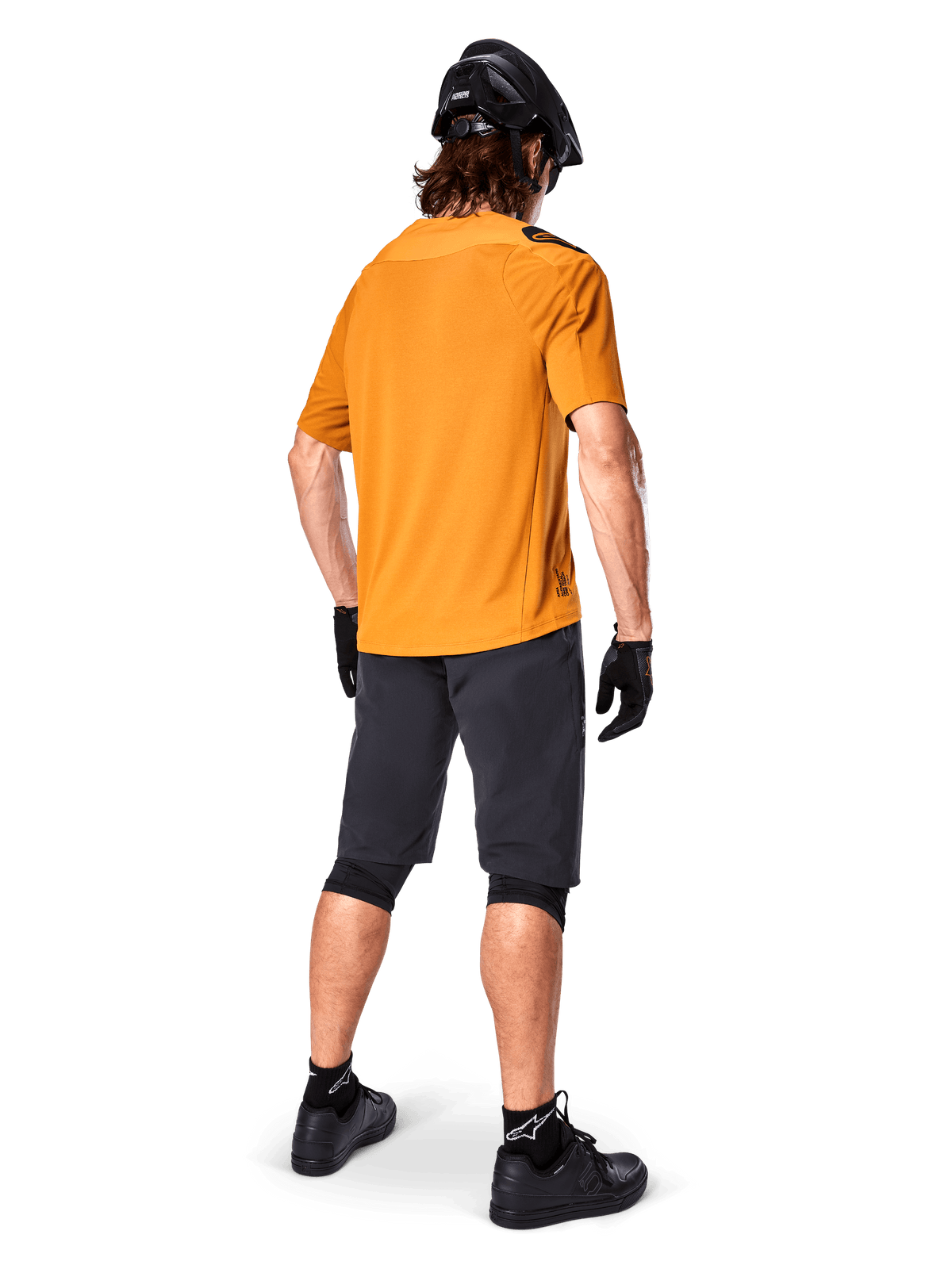 Alpinestars A-Aria Polartec Switch Trikot, kurzärmeliges MTB-Trikot, Dunkelgold, Rückansicht eines Models in dunkelgrauen Mountainbike-Shorts, schwarzem Helm und Handschuhen, technische Radsportbekleidung für Offroad-Trails