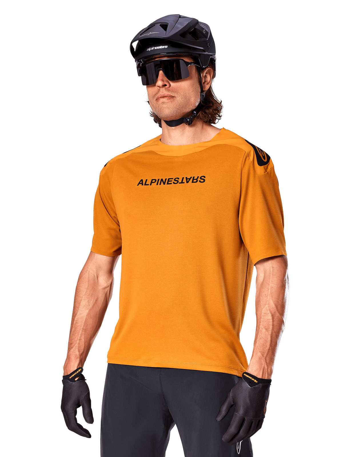 Alpinestars A-Aria Polartec Switch Trikot, Kurzarm-MTB-Trikot, Dunkelgold mit schwarzem Branding, getragen von Model mit schwarzem Helm, Sonnenbrille und Radhandschuhen, Hochleistungs-Mountainbike-Bekleidung