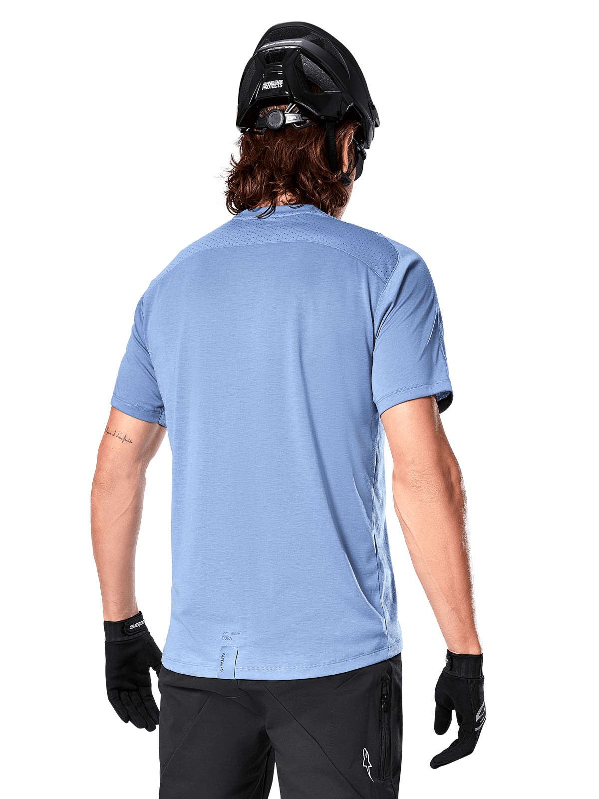 Alpinestars A-Dura Dri Astar Kurzarmtrikot, MTB-Trikot, Infinity Blue, Rückansicht mit Mesh-Belüftungseinsätzen an den Schultern und verlängertem Rücken, kombiniert mit schwarzem MTB-Helm und Handschuhen, Performance-Radbekleidung