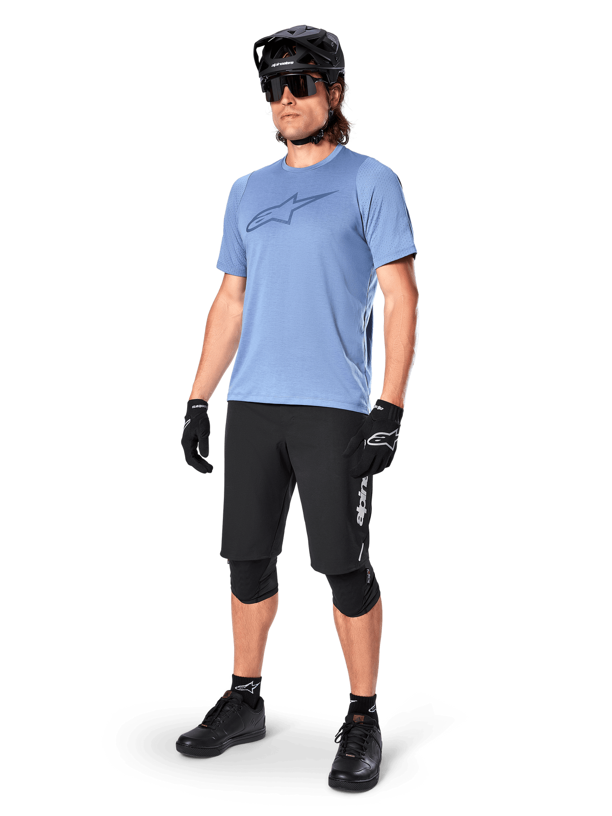 Männlicher Fahrer im Alpinestars A-Dura Dri Astar Kurzarmtrikot in Infinity Blue, kombiniert mit schwarzen MTB-Shorts, schwarzem Helm, Sonnenbrille, Knieschützern und Handschuhen, komplettes Mountainbike-Outfit