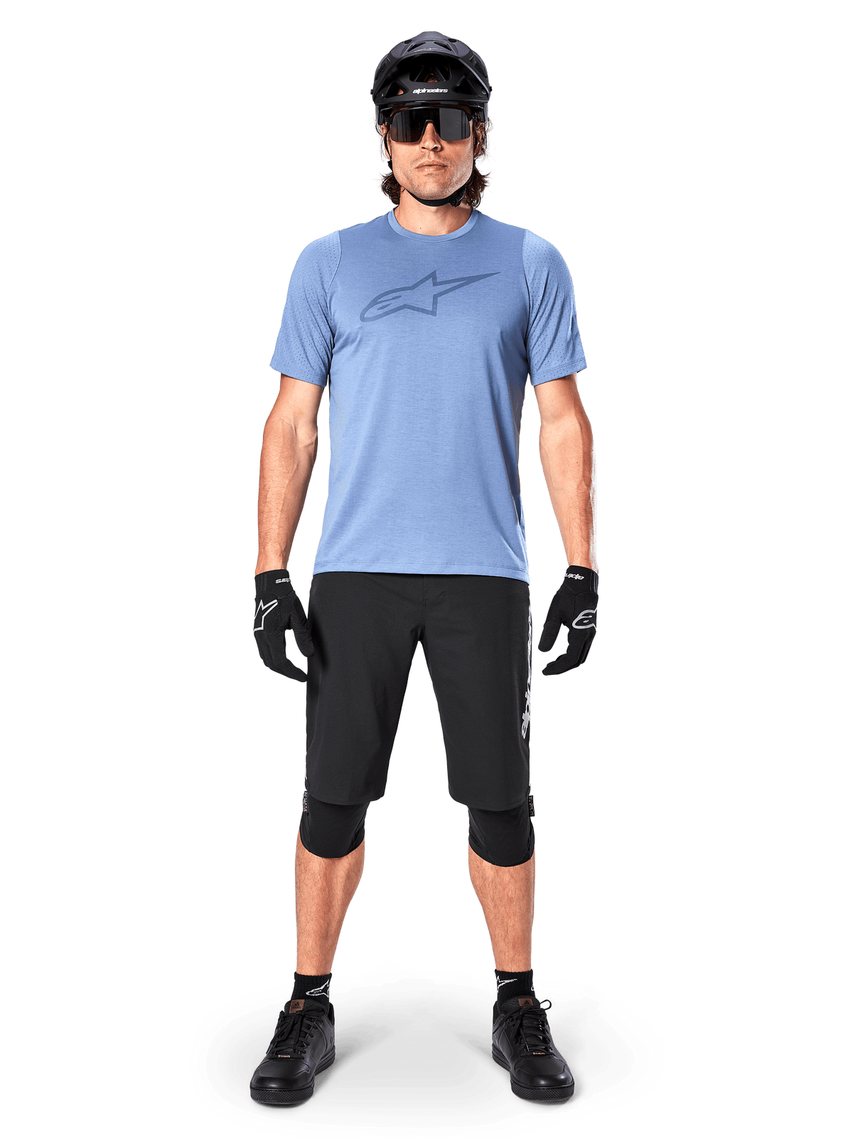Männlicher Mountainbike-Fahrer im Alpinestars A-Dura Dri Astar Kurzarmtrikot in Infinity Blue, mit markantem Astars-Logo auf der Brust, kombiniert mit schwarzen MTB-Shorts, schwarzem Helm, Sonnenbrille und Schutzausrüstung für Geländefahrten