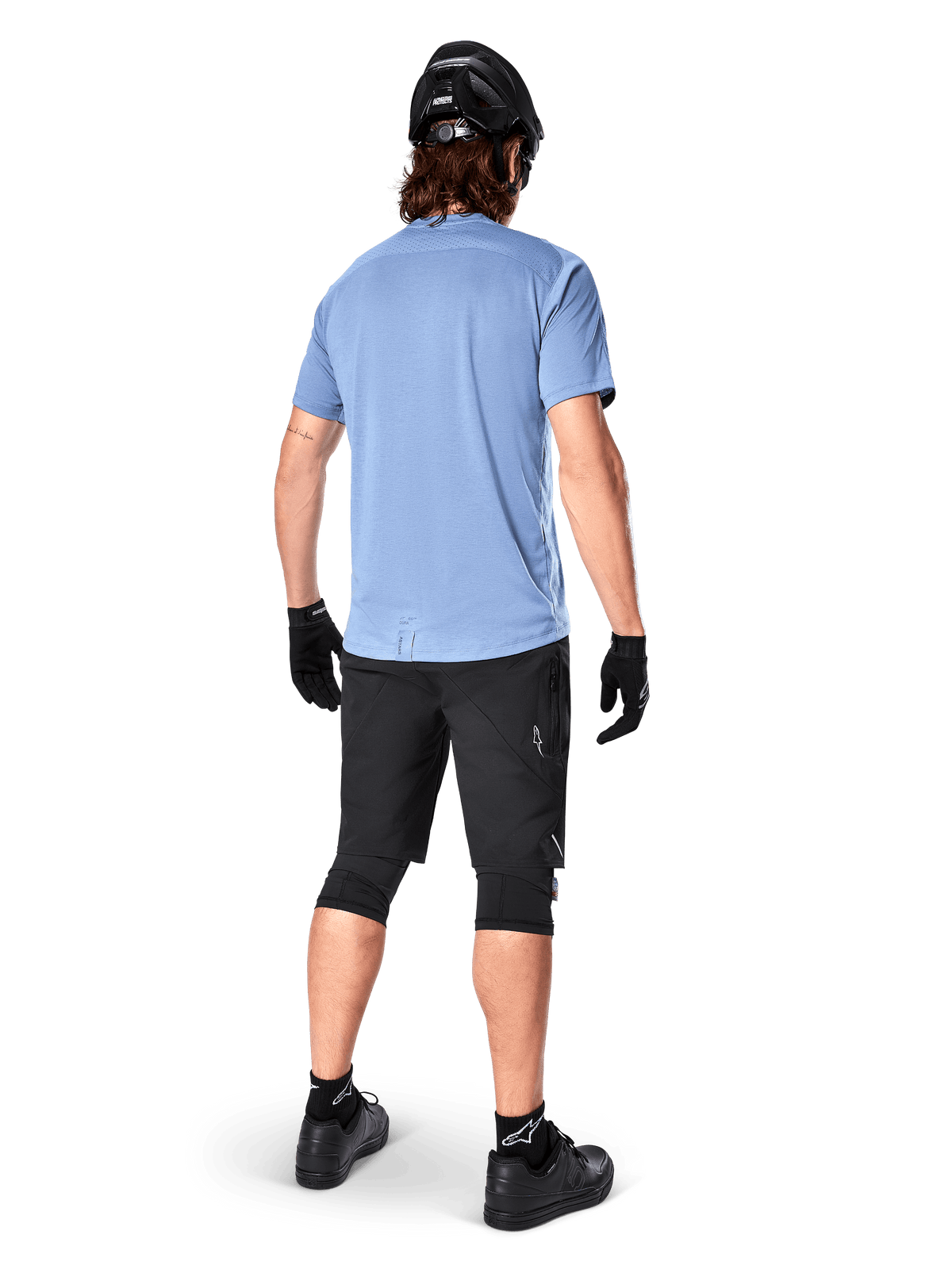 Alpinestars A-Dura Dri Astar Kurzarmtrikot, Infinity Blue, Rückansicht, kombiniert mit schwarzen Mountainbike-Shorts und Helm, technische Radsportbekleidung mit feuchtigkeitsableitendem Material und verlängertem Rückenteil