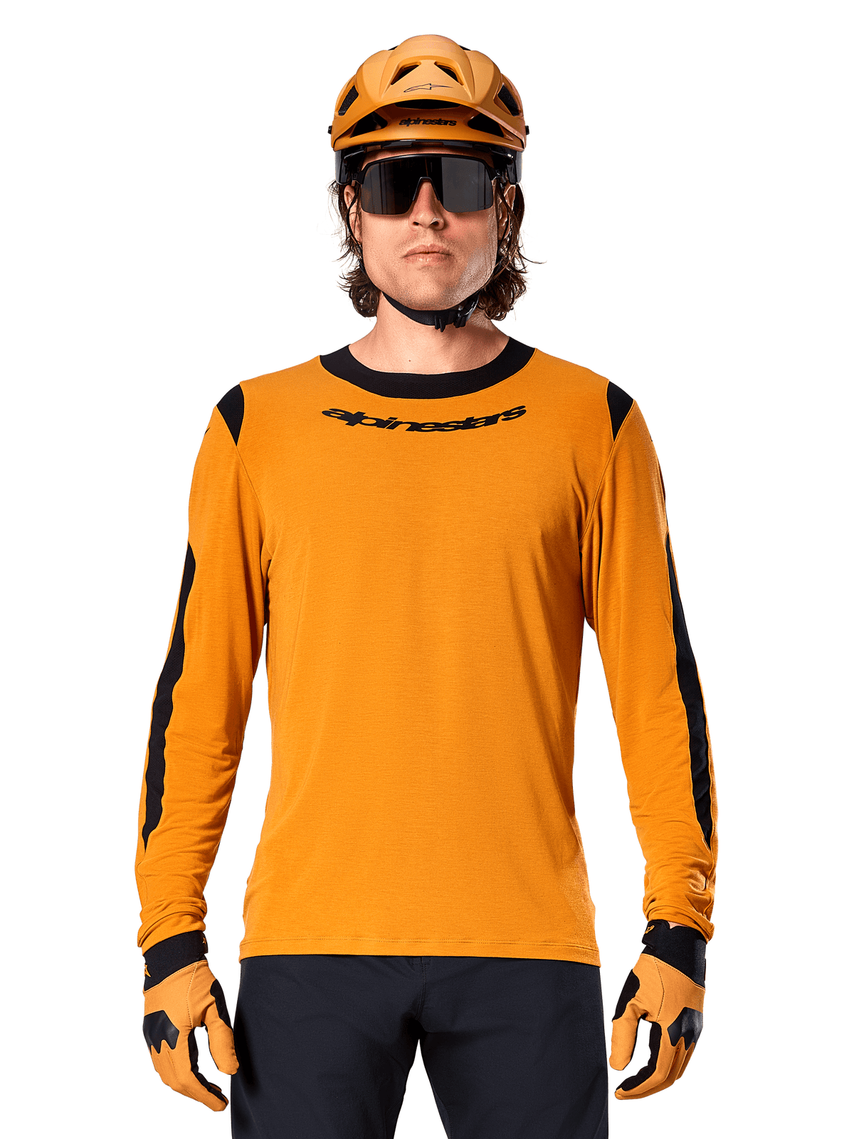 Männliches Model im Alpinestars A-Dura Dri Wool Langarmtrikot in Dark Gold, kombiniert mit einem passenden goldenen MTB-Helm und Handschuhen, schwarze Mesh-Einsätze an Schultern und Ärmeln, schwarzer Alpinestars-Schriftzug auf der Brust, dunkle Sonnenbrille und Hose, technische Mountainbike-Bekleidung