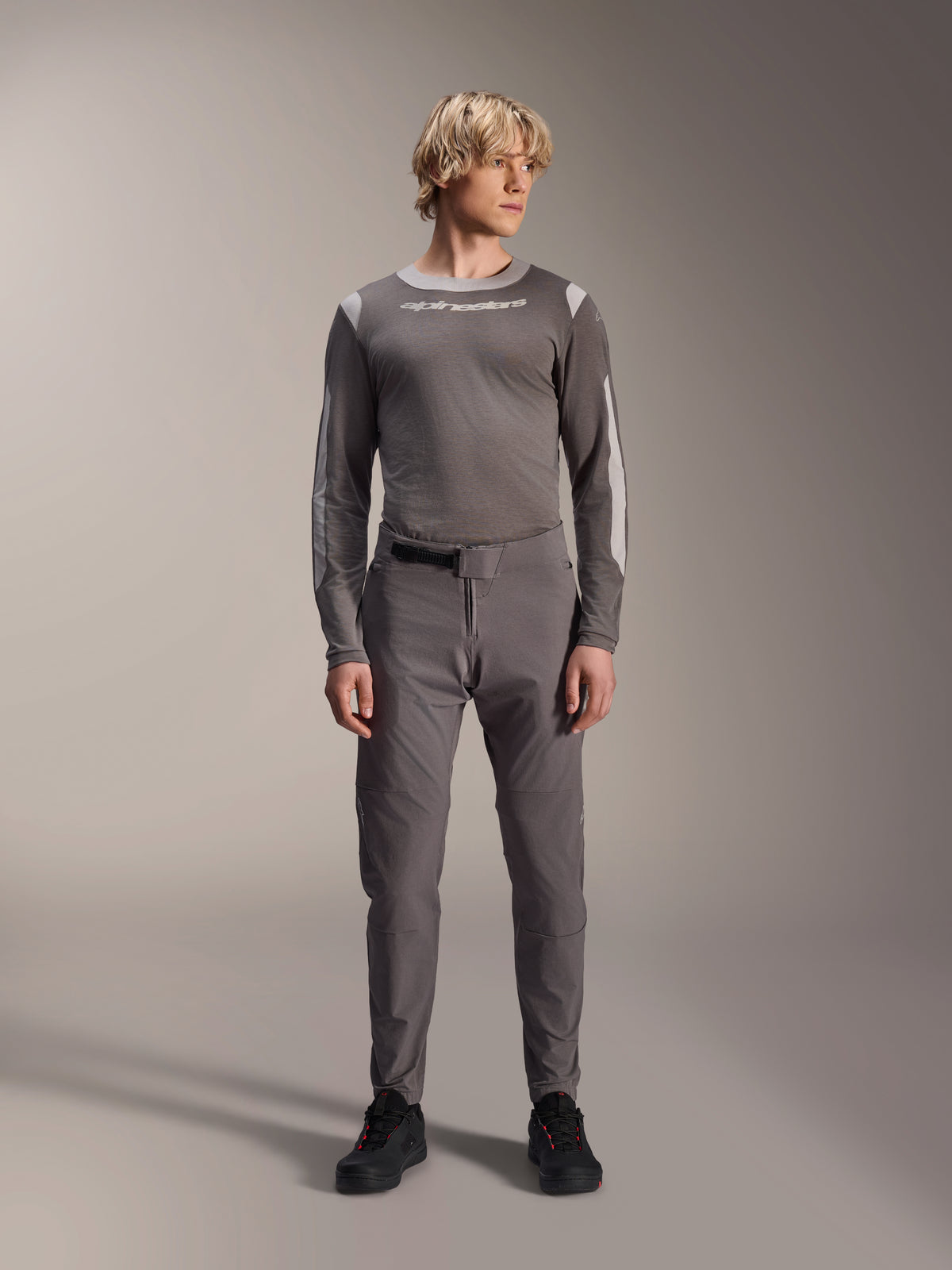 Alpinestars A-Dura Elite Hose, dunkelgraue Mountainbike-Hose, Ganzkörperansicht, kombiniert mit einem passenden grauen Langarm-Performance-Trikot mit Alpinestars-Logo, schwarze Schuhe mit roten Akzenten, sportliches Radsport-Outfit