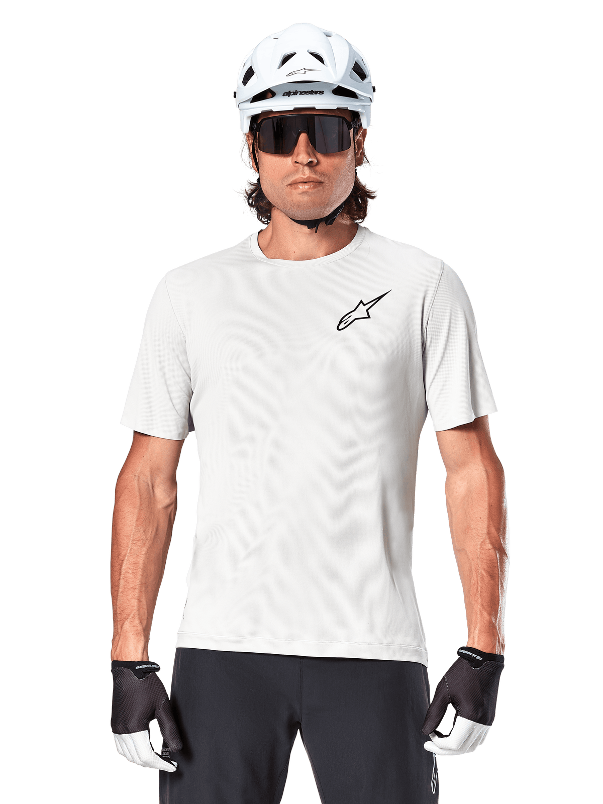 Radfahrer trägt Alpinestars A-Aria Astar Kurzarmtrikot, White Dove mit kleinem schwarzem Astar-Logo auf der Brust, weißer Fahrradhelm, schwarze Sonnenbrille und schwarz-weiße Handschuhe, Performance-MTB-Ausrüstung für Offroad-Fahrten