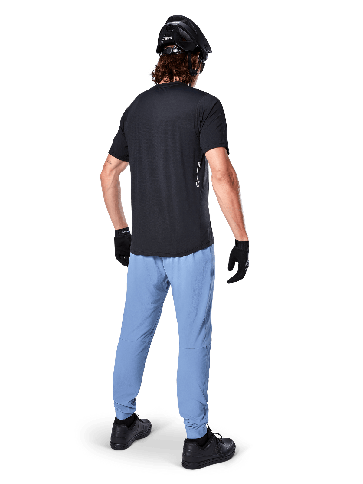 Alpinestars A-Dura Oscar Jersey - Short Sleeve, Black, Rear view of rider wearing a black mountain bike jersey, paired with light blue pants, black helmet, and black gloves, technical MTB apparel for off-road performance