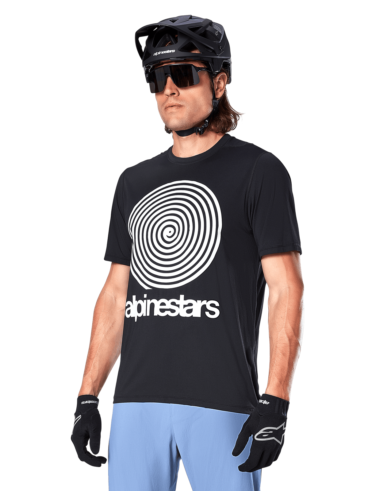 Alpinestars A-Dura Oscar Jersey - Short Sleeve, Black, featuring a large white spiral graphic and Alpinestars branding on the chest, worn by a rider with a black MTB helmet, sunglasses, and light blue pants