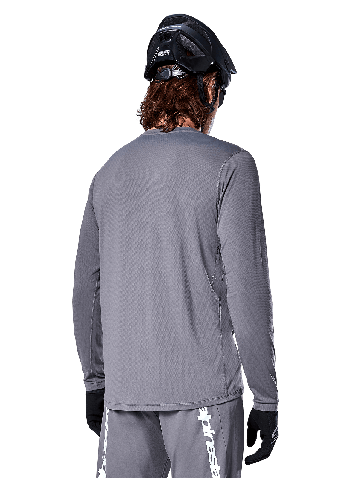 Alpinestars A-Dura Rocker Long Sleeve Jersey in Dark Gray, back view of mountain bike rider, paired with matching gray shorts featuring white branding, black MTB helmet, and black gloves, professional off-road cycling gear.