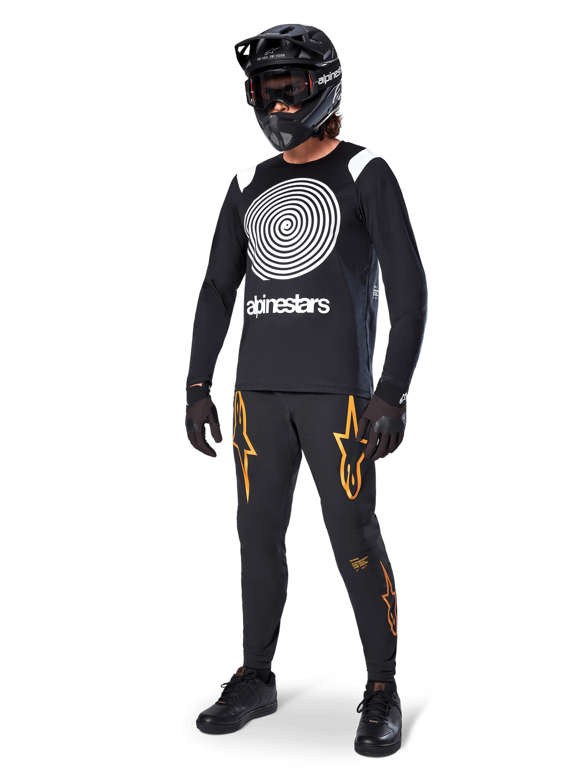 MTB-Fahrer im Alpinestars A-Supra Oscar Langarm-Trikot in Schwarz, weiße Vintage-Oscar-Spiralgrafik, schwarze Hose mit orangefarbenen Stern-Logos, schwarzer Fullface-Helm mit Goggles, schwarze Handschuhe, professionelle Mountainbike-Ausrüstung