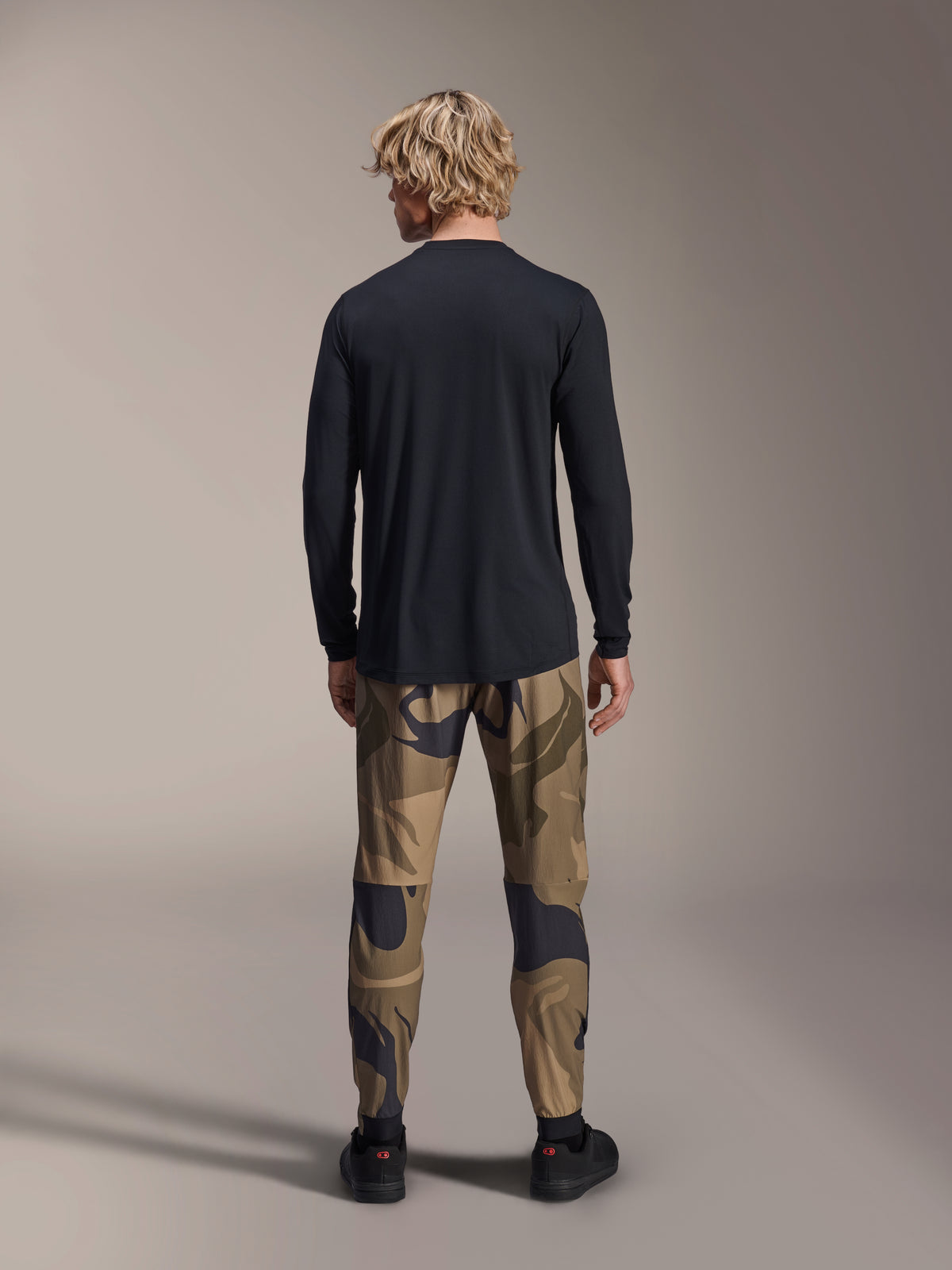 Alpinestars A-Dura Astar Langarmtrikot, Schwarz, Rückansicht eines Modells in Camouflage-Hose, mit verlängertem Saum und regulärer Passform für Mountainbiking