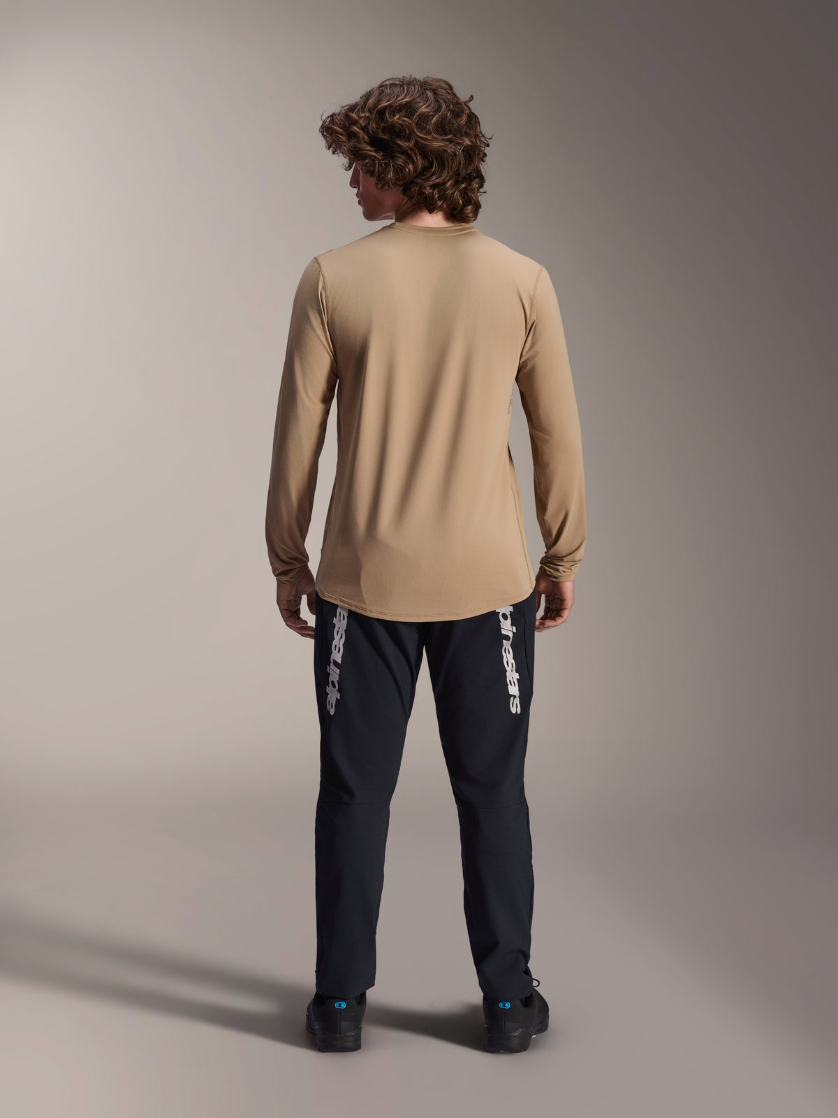 Alpinestars A-Dura Astar Long Sleeve Jersey, Light Brown, back view showing the longer drop tail, worn with black pants featuring Alpinestars branding, performance mountain bike apparel