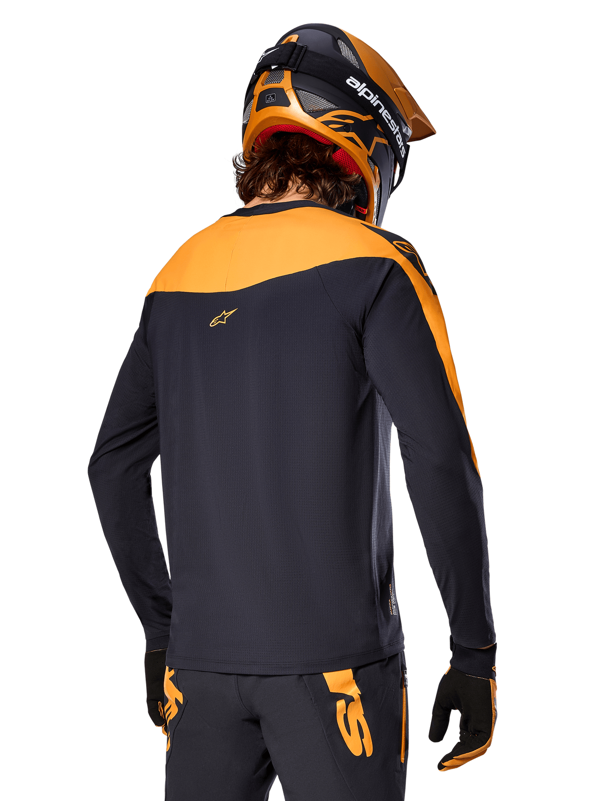 Alpinestars A-Supra Race Trikot – Langarm, Schwarz und Orange, Rückansicht eines Fahrers mit passendem Helm und Mountainbike-Hose, Performance-Passform mit mikroperforierter Textur, professionelle MTB-Rennausrüstung