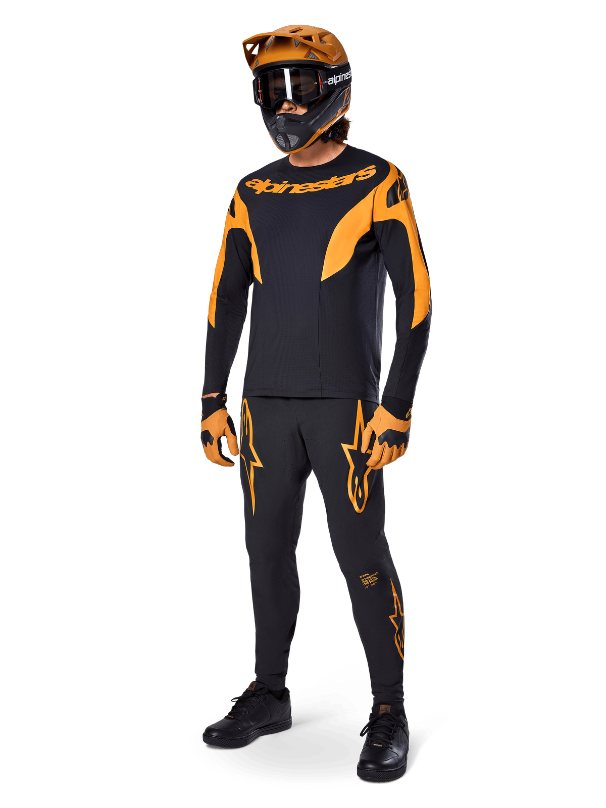MTB-Fahrer in kompletter Rennausrüstung, schwarzes A-Supra Race Jersey mit orangefarbenen Akzenten, passende schwarze Hose mit orangefarbenen Alpinestars-Logos, orange-schwarzer Full-Face-Helm mit Brille, orange-schwarze Handschuhe, abgestimmtes Outfit für Mountainbike-Rennen