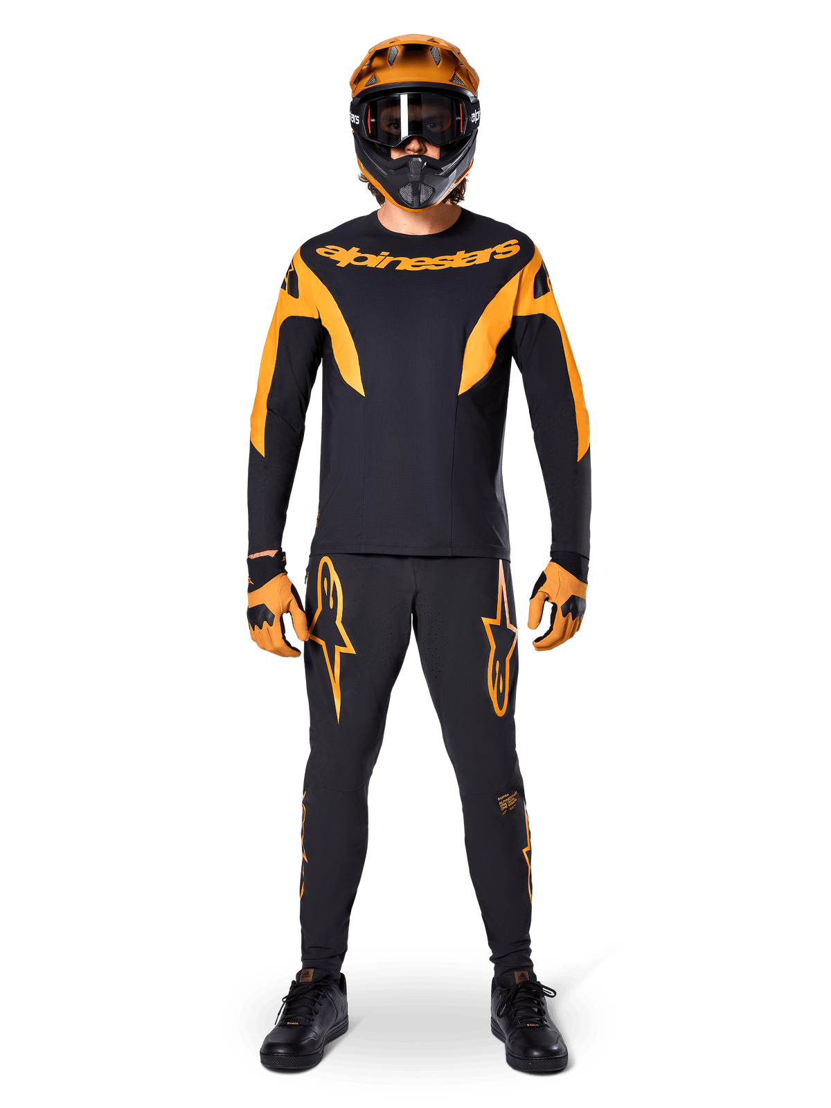 MTB-Fahrer im Alpinestars A-Supra Race Trikot – Langarm in Schwarz und Orange, passender schwarz-orangefarbener Hose, Handschuhen und Fullface-Helm mit Goggle, koordiniertes Mountainbike-Set für Renneinsätze und Offroad-Performance
