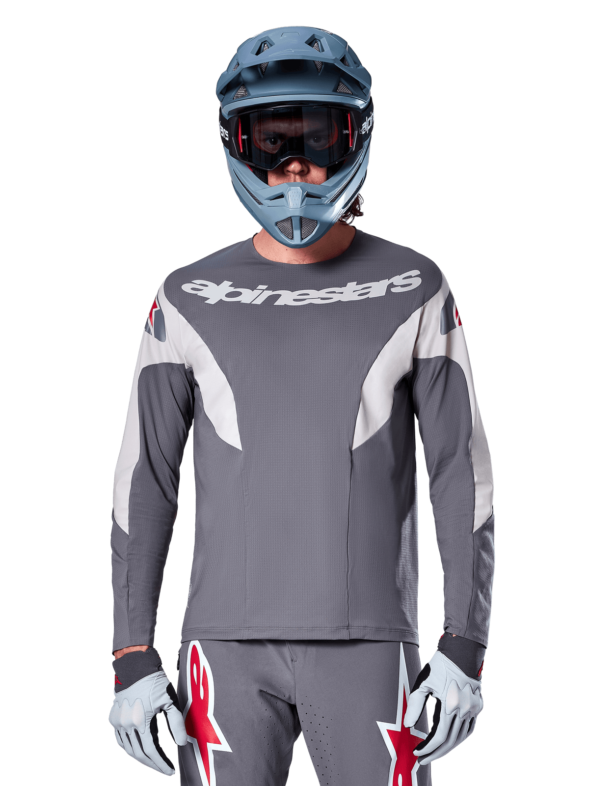 MTB-Fahrer im Alpinestars A-Supra Race Trikot – Langarm in Dunkelgrau, langärmeliges Radsport-Trikot mit weißem Alpinestars-Branding, kombiniert mit einem blau-grauen Fullface-Helm, einer Goggle und grauen Rennhandschuhen, komplette Mountainbike-Rennausrüstung für Offroad-Performance