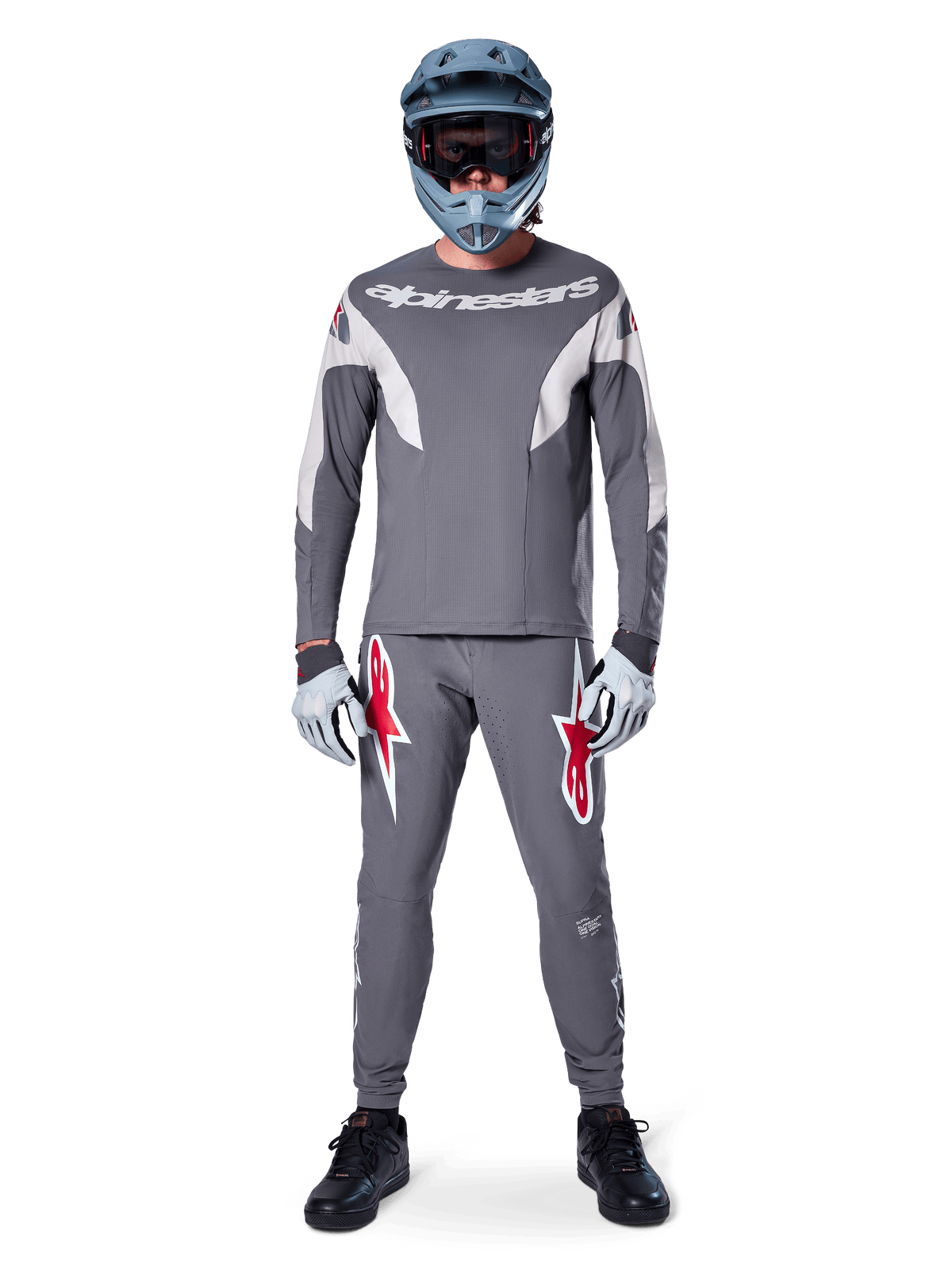 Fahrer im Alpinestars A-Supra Race Trikot – Langarm in Dunkelgrau, kombiniert mit passender grauer Hose mit auffälligen roten Stern-Logos, grauem Helm mit Goggle und hellgrauen Handschuhen, komplette MTB-Rennausrüstung für Performance-Offroad-Radsport