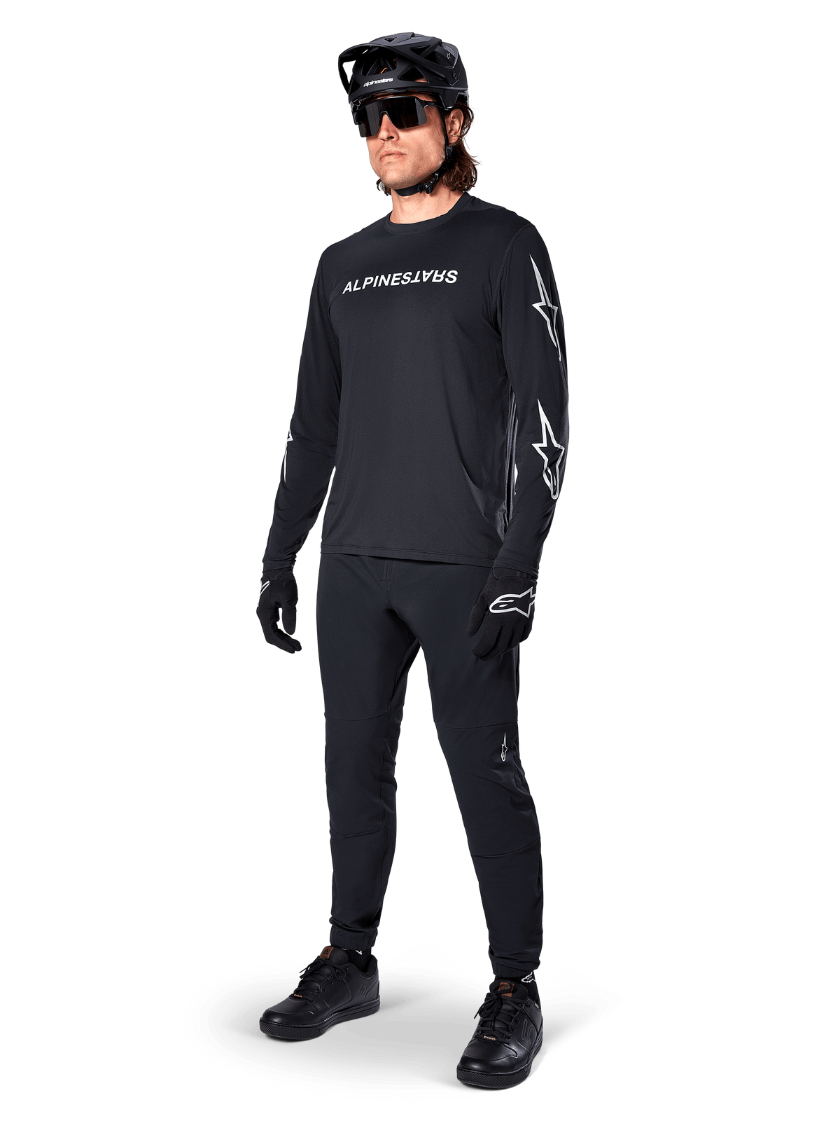 Alpinestars A-Dura Switch Langarmtrikot, Schwarz, Mountainbike-Trikot getragen mit schwarzer Hose, Helm und Handschuhen, mit weißem Wortmarken-Logo auf der Brust und Stern-Logos auf den Ärmeln, abgestimmte MTB-Ausrüstung für Offroad-Fahrten