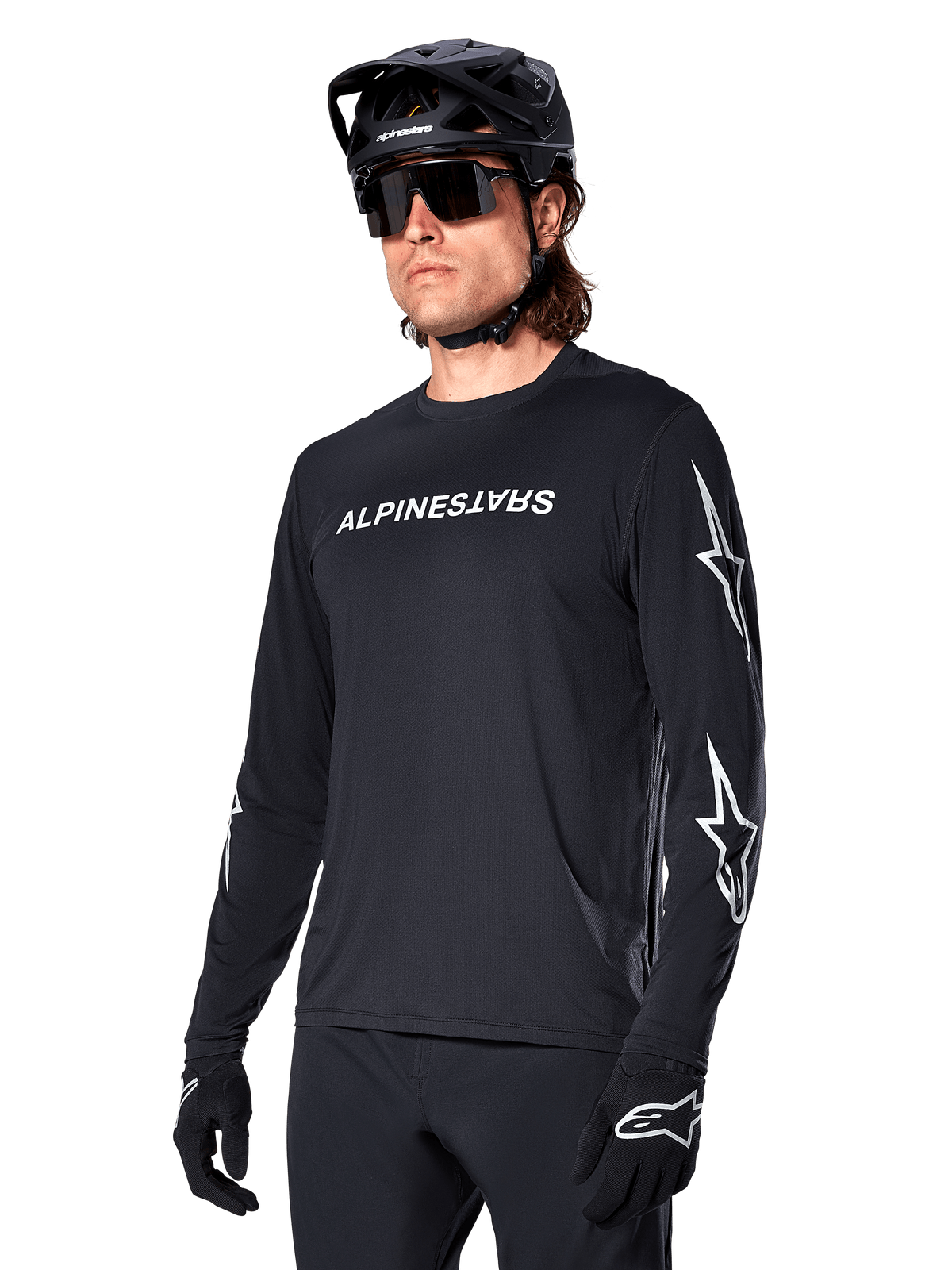 Männlicher Radfahrer im Alpinestars A-Dura Switch Langarmtrikot, Schwarz mit weißem Schriftzug und Stern-Logos auf den Ärmeln, kombiniert mit schwarzem MTB-Helm und Sonnenbrille, Hochleistungs-Radsportausrüstung für Offroad-Fahrten