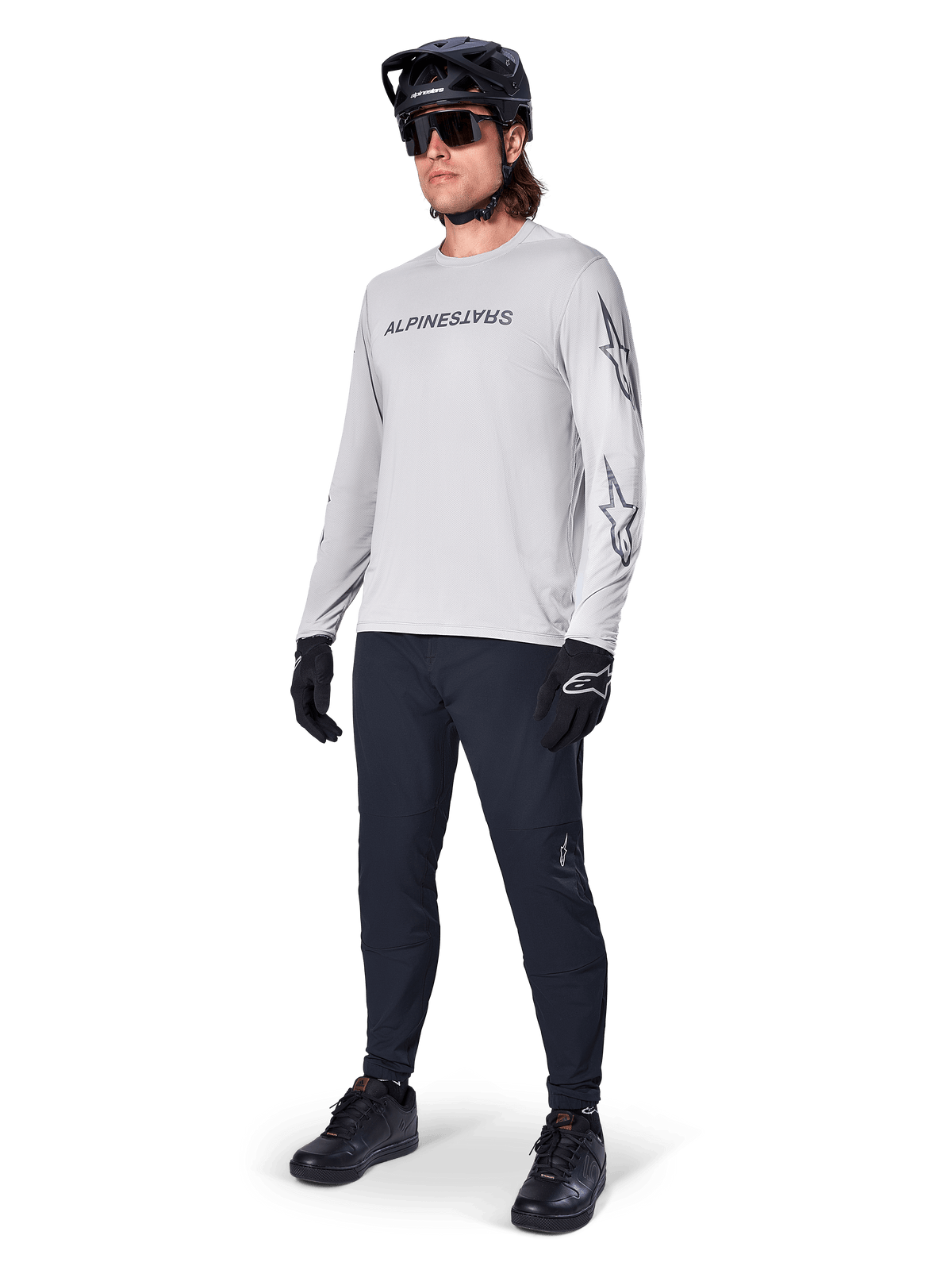 Alpinestars A-Dura Switch Long Sleeve Jersey, Light Gray, worn by male rider with black mountain bike pants and helmet, featuring black wordmark logo on chest and star graphics on sleeves, performance off-road cycling gear