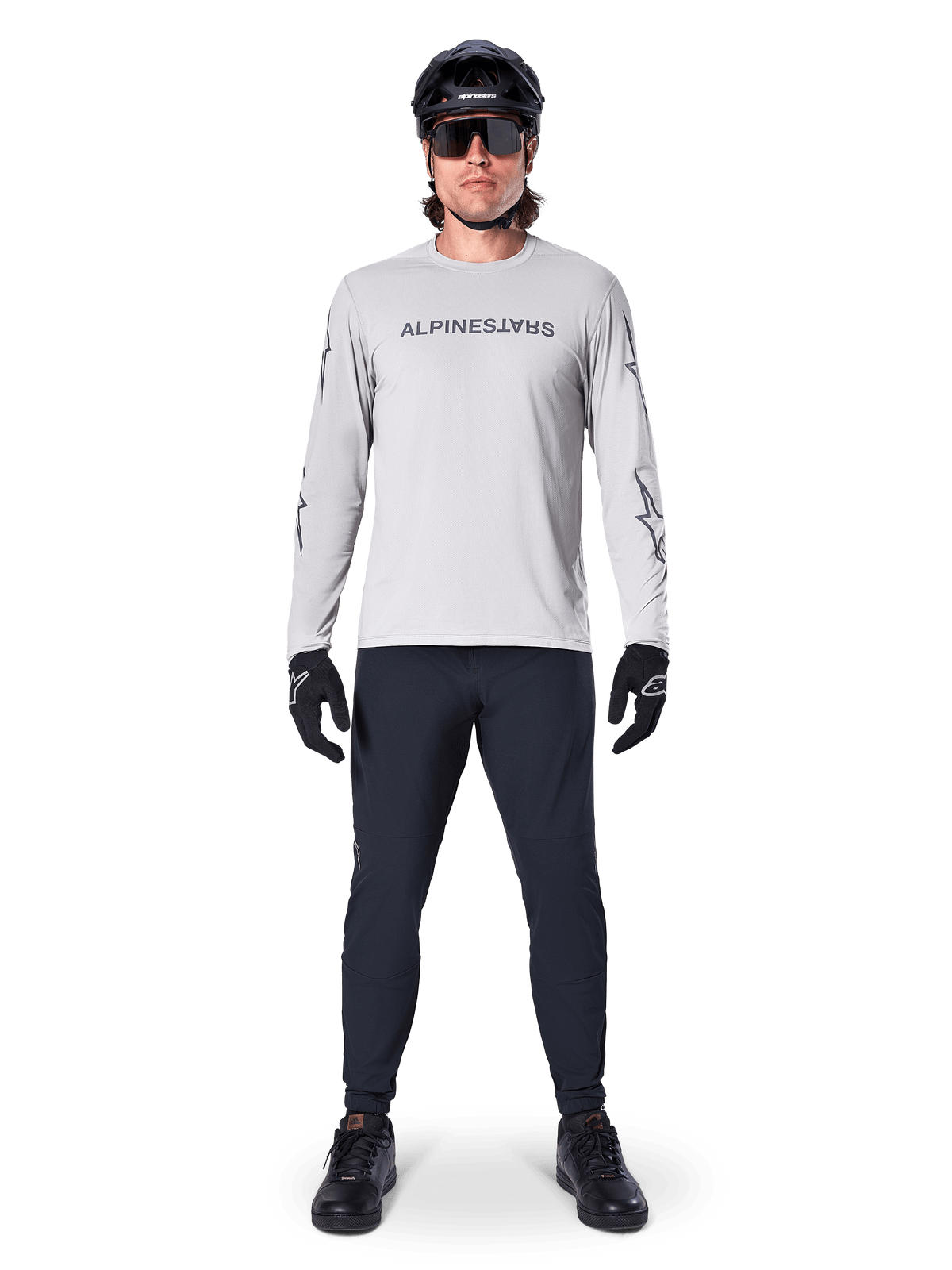 Alpinestars A-Dura Switch Long Sleeve Jersey in Light Gray, featuring a stylized wordmark logo on the chest, worn with black pants, helmet, and gloves, performance mountain bike apparel for off-road cycling