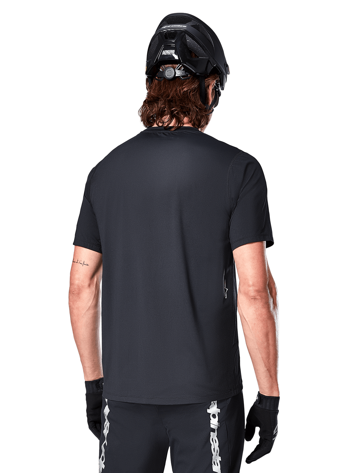 Alpinestars A-Dura Switch Kurzarmtrikot, Schwarz, Rückansicht eines Models mit schwarzem Fahrradhelm und MTB-Shorts, hebt die reguläre Passform und den verlängerten Rücken für das Mountainbiken hervor.