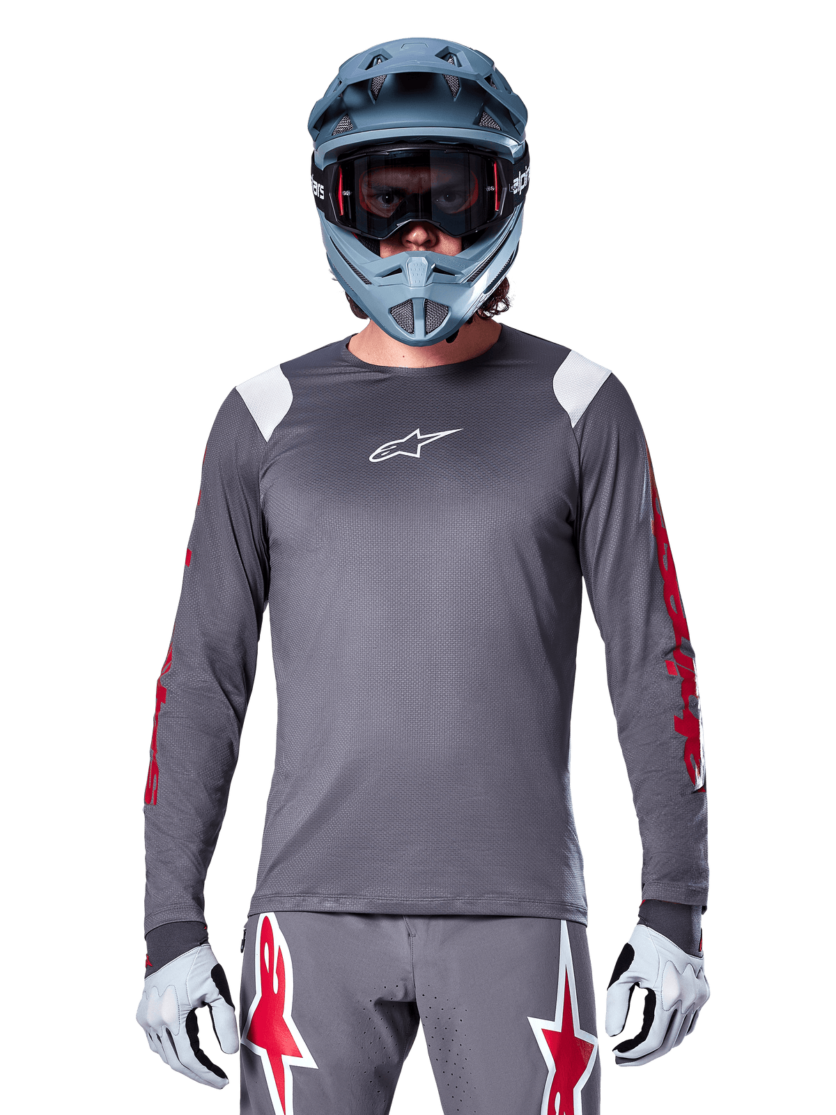 MTB-Fahrer im Alpinestars A-Supra Astar Langarmtrikot, Dunkelgrau mit roten Grafiken an den Ärmeln und weißen Schulterakzenten, passender grauer Hose mit roten Stern-Logos, blauem Fullface-Helm und Goggle, abgestimmte Offroad-Radsportausrüstung
