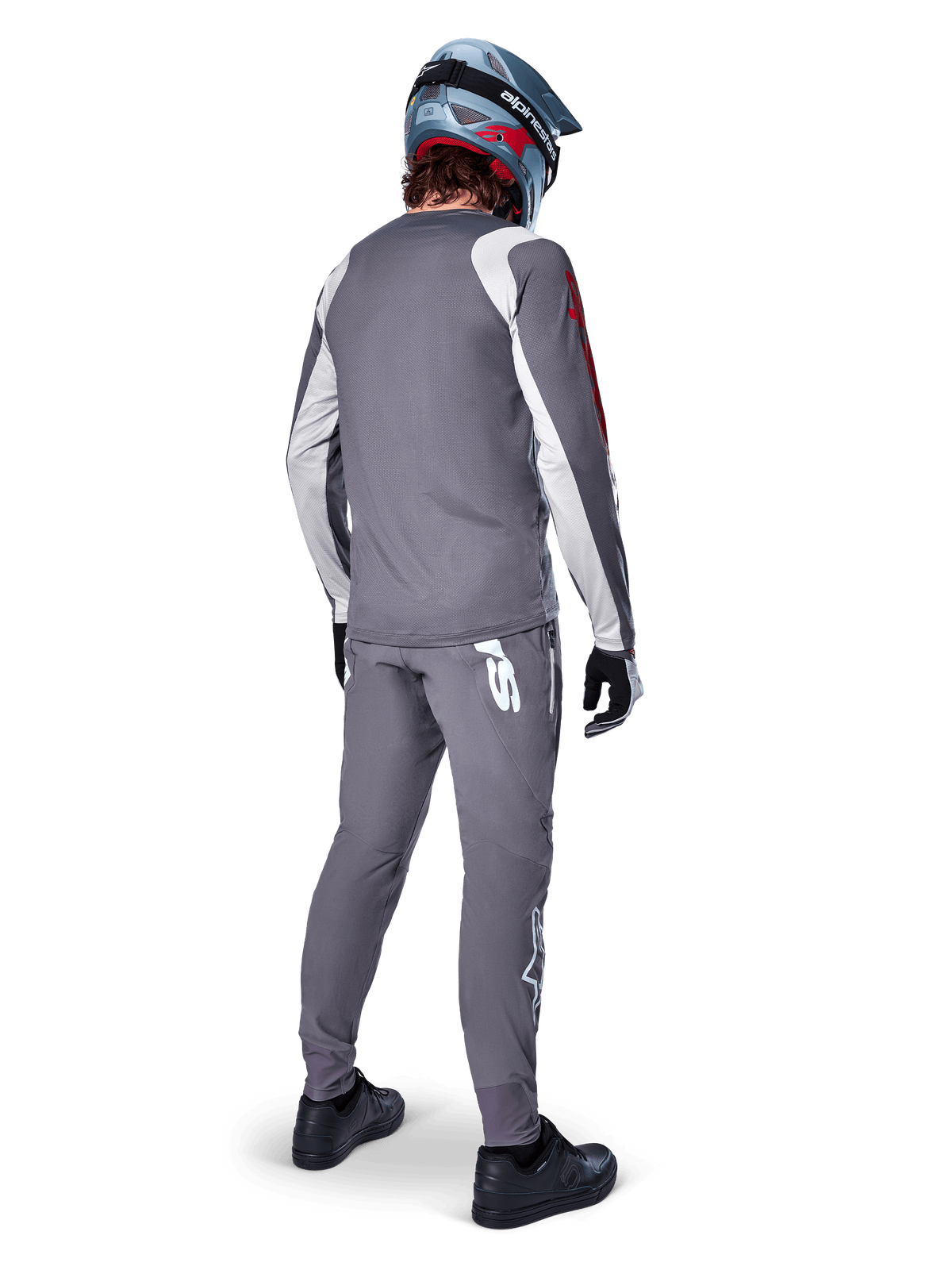 Alpinestars A-Supra Astar Trikot, Langarm-MTB-Trikot, Dunkelgrau mit weißen Ärmelakzenten und rotem Logo, Rückansicht eines Fahrers in passender grauer Hose und blauem Full-Face-Helm, Performance-Radsportbekleidung