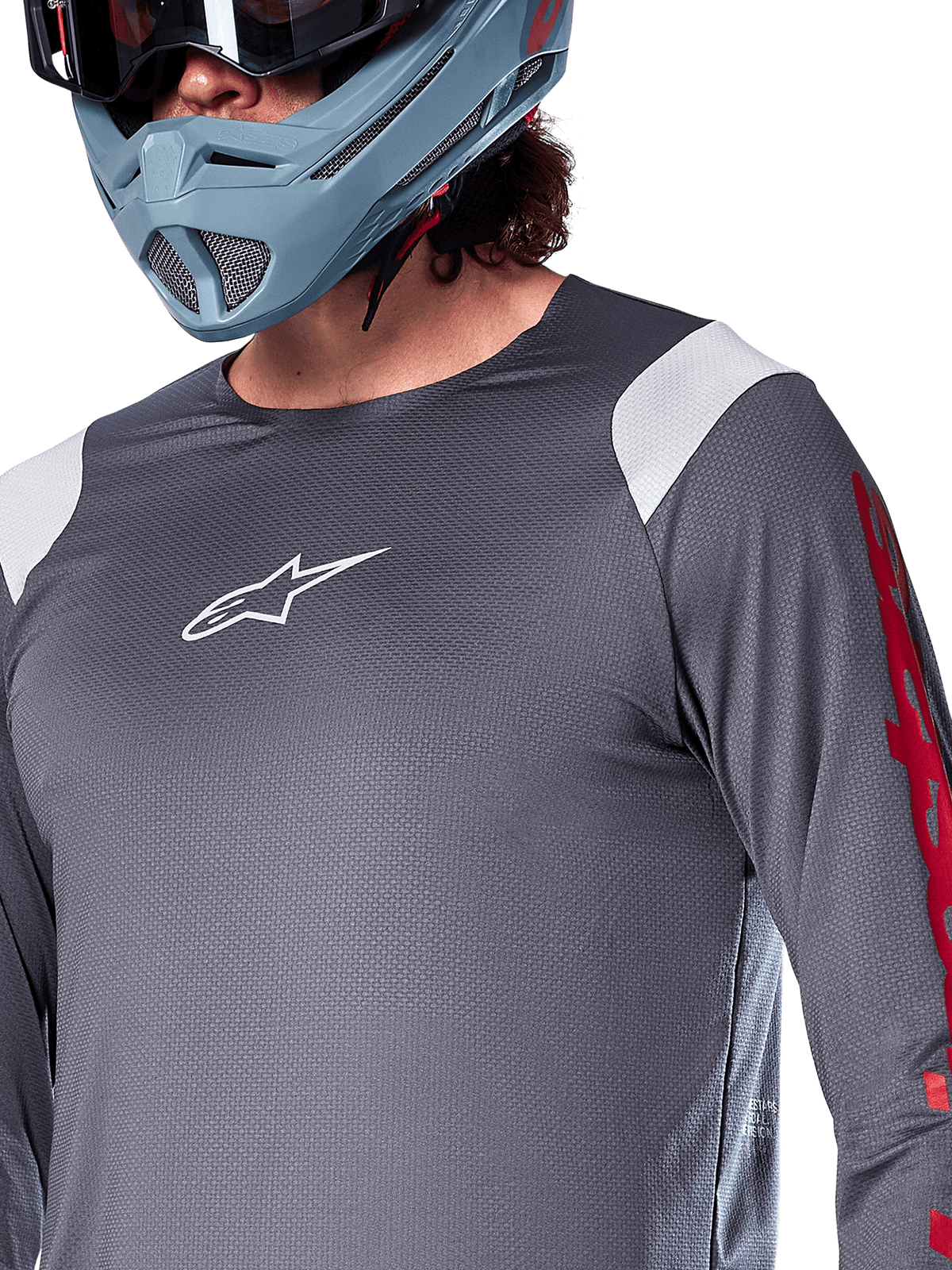 Alpinestars A-Supra Astar Langarmtrikot, Dunkelgrau mit weißen Schultereinsätzen und roten Grafiken am Ärmel, getragen mit einem hellblau-grauen Full-Face-Helm, Performance-Mountainbike-Bekleidung