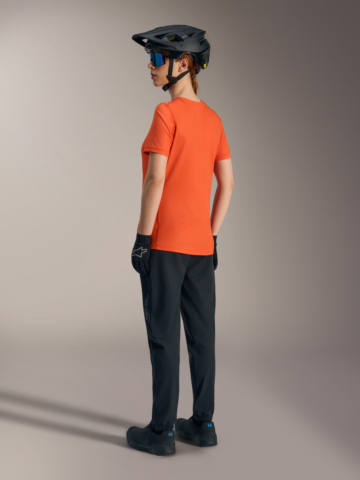 Orange Alpinestars Stella A-Dura Ride short sleeve jersey for women, back view with black MTB pants and helmet.