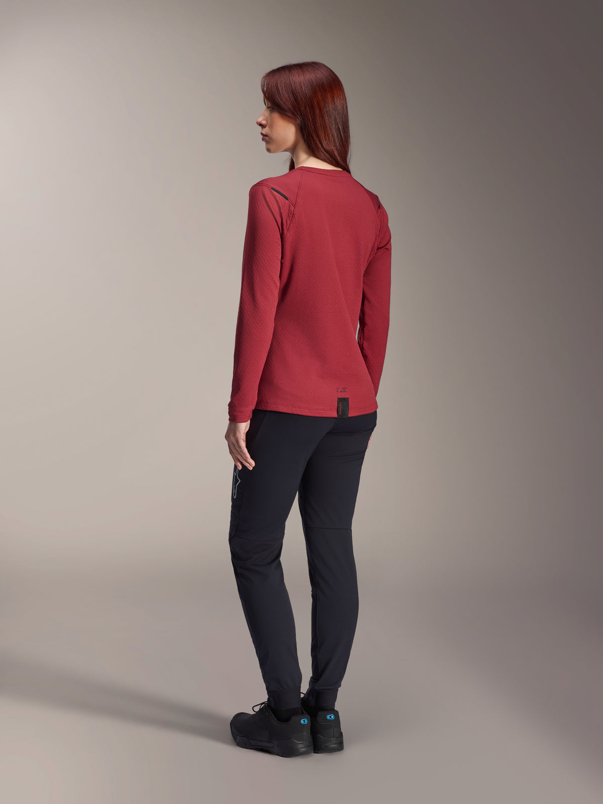 Alpinestars Stella A-Dura Thermohose in Schwarz, kombiniert mit einem roten langärmeligen Thermo-Jersey und schwarzen Schuhen, Rückansicht, Mountainbike-Bekleidung für Fahrten bei kaltem Wetter.