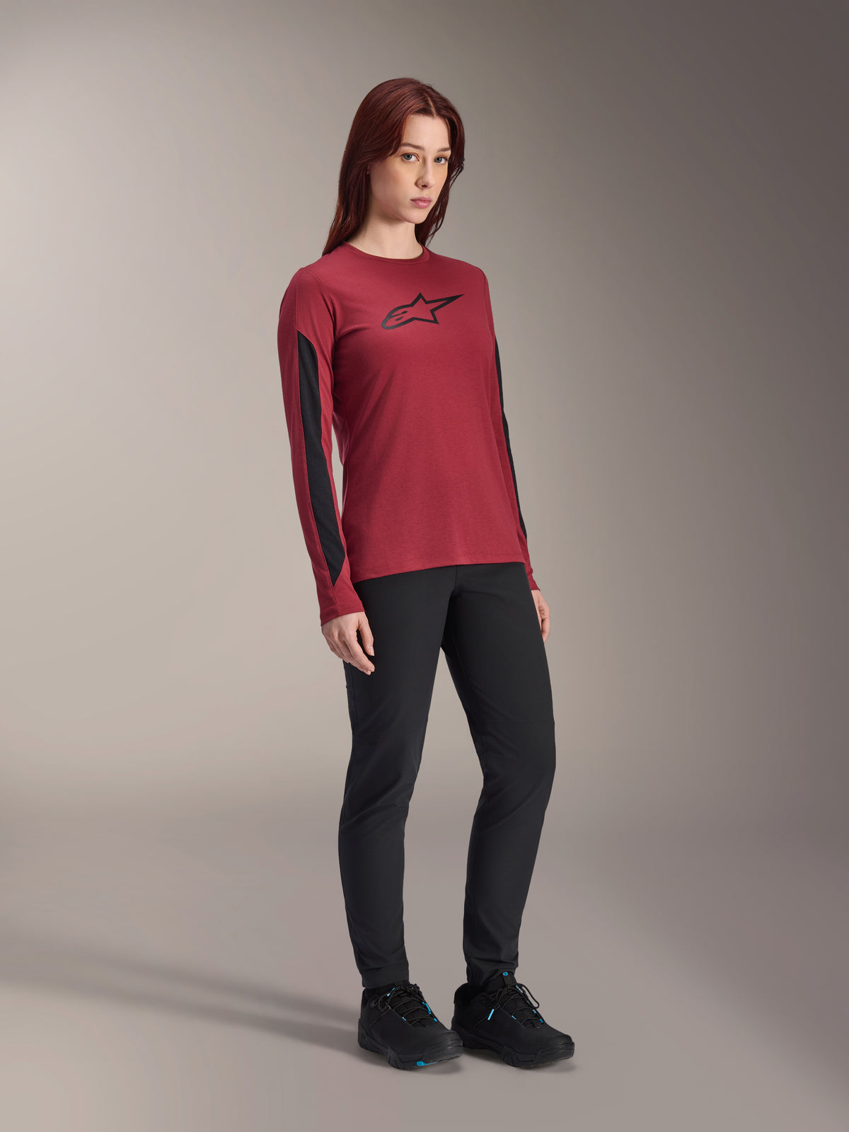 Alpinestars Stella A-Dura Dri Astar Langarmtrikot für Damen, Burgundrot mit schwarzem Brustlogo und schwarzen Mesh-Einsätzen an den Ärmeln, kombiniert mit schwarzer technischer Hose und schwarzen Radschuhen, Hochleistungs-Mountainbike-Bekleidung für Damen