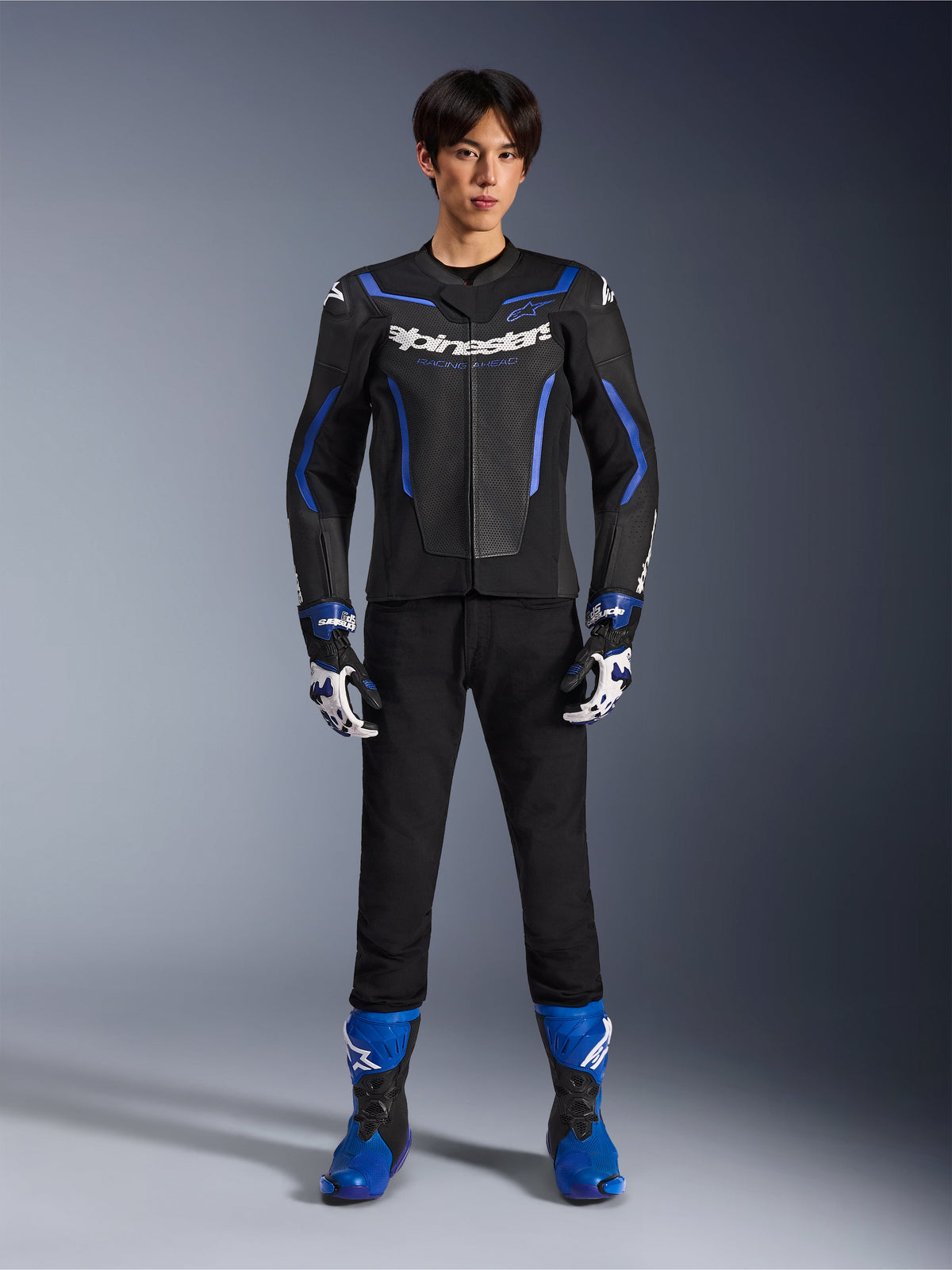 Alpinestars GP Force V2 Airflow Lederjacke in Schwarz Metallic Blau, getragen mit passenden Rennhandschuhen, schwarzer Hose und blauen Stiefeln, professionelle Sport-Motorradausrüstung, Ganzkörper-Studioaufnahme